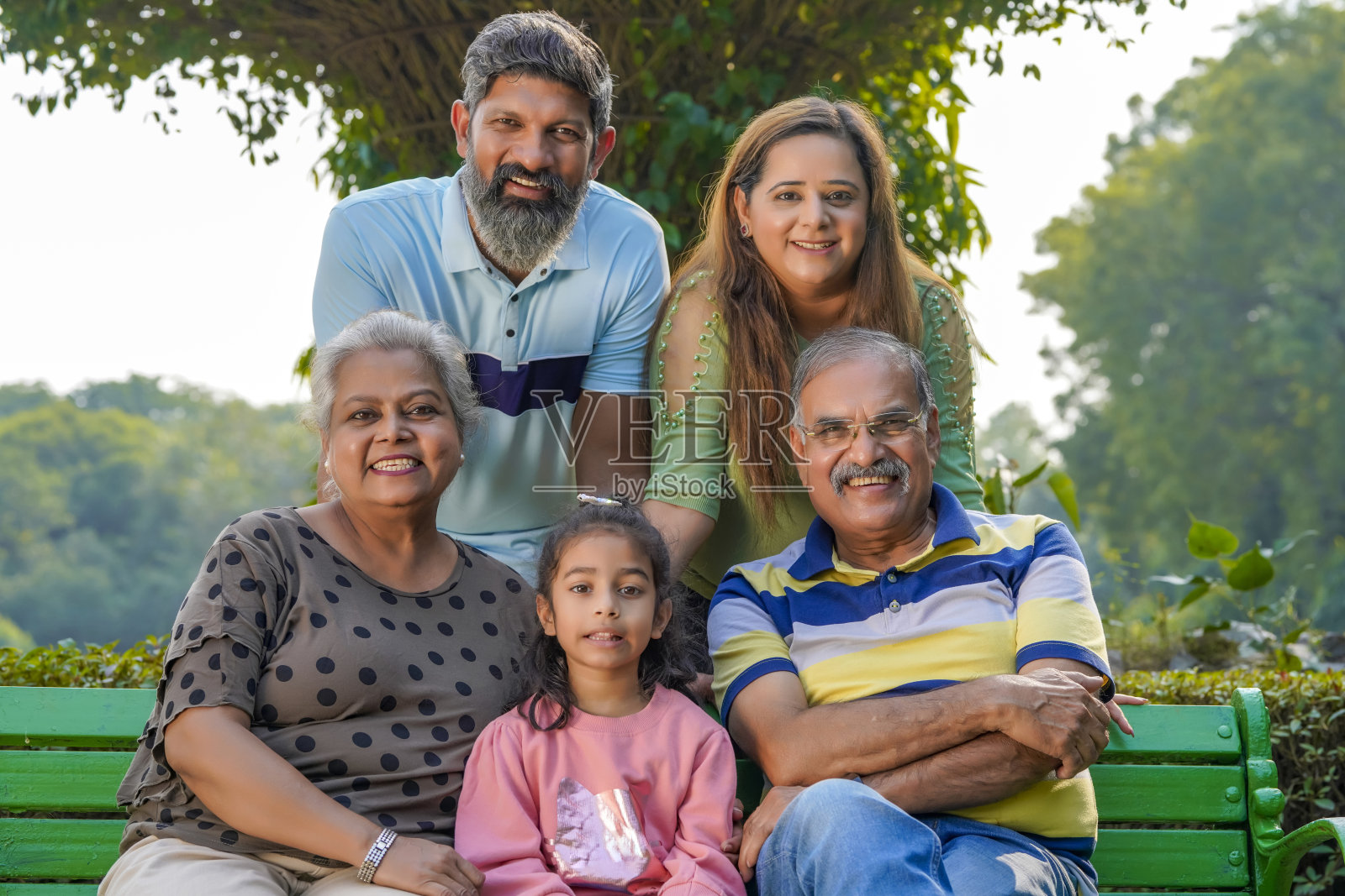 快乐的印度或亚洲家庭坐在公园里。照片摄影图片