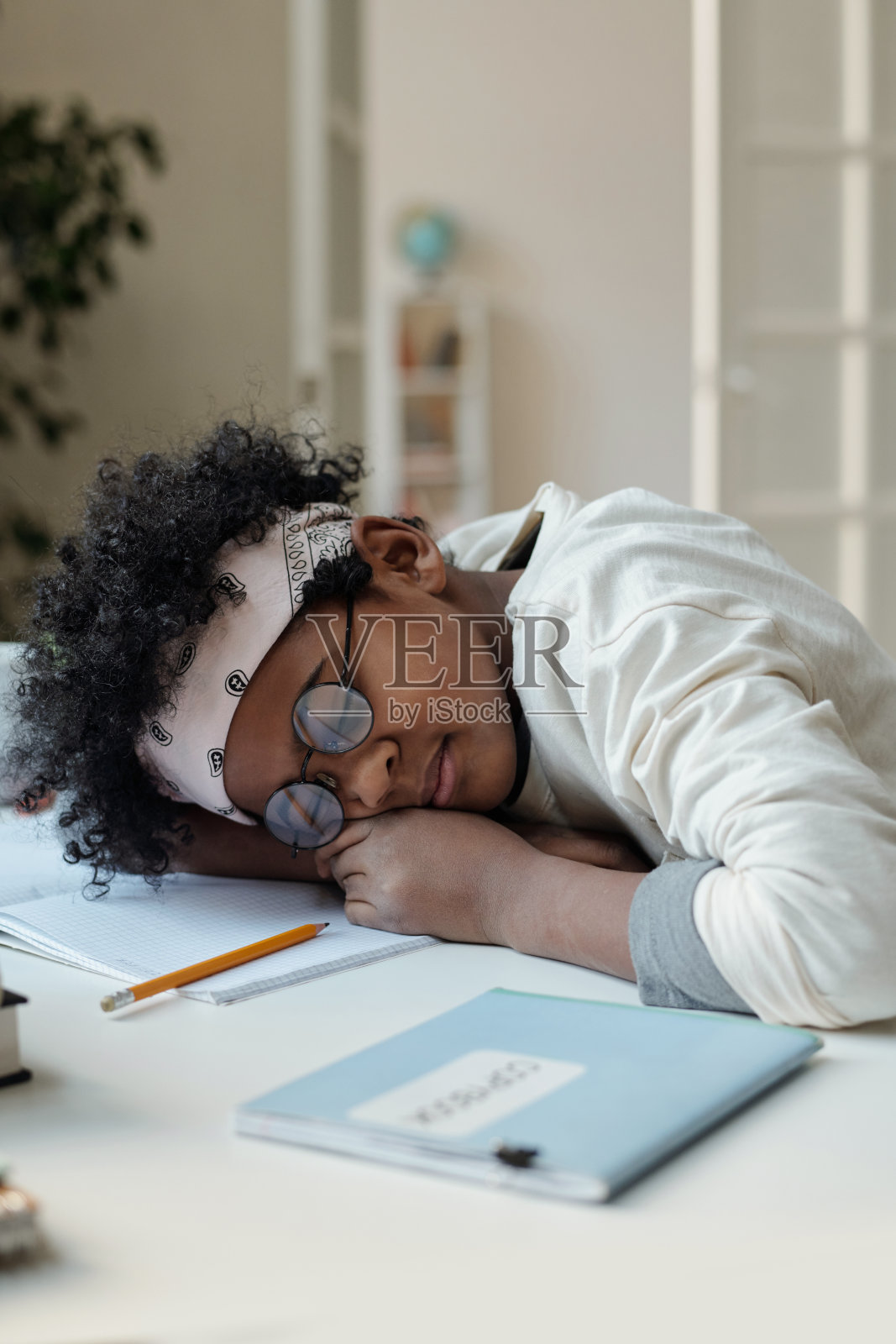 可爱的小学生在书桌前打盹，同时保持头在打开的抄写本上照片摄影图片