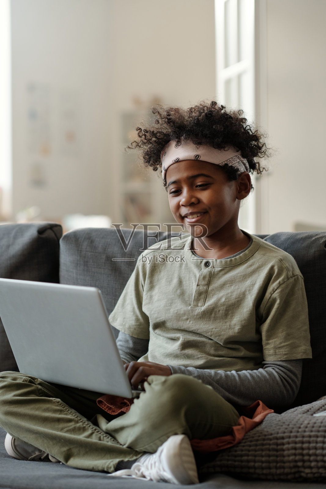 可爱的微笑男孩在灰色家居服坐在沙发上在客厅照片摄影图片