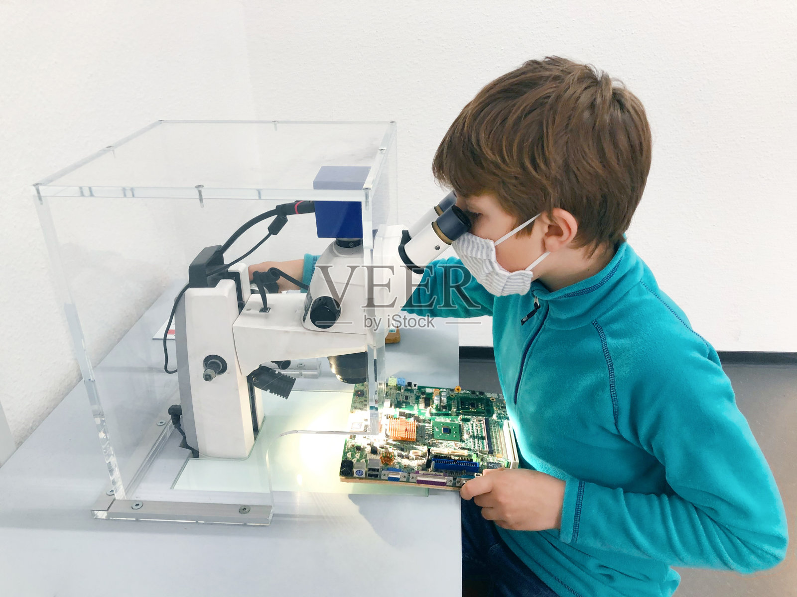 小男孩在学校实验室用显微镜做实验。好奇的孩子学习物理和计算机方案。由于冠状病毒大流行，一名学生戴着医用口罩。照片摄影图片