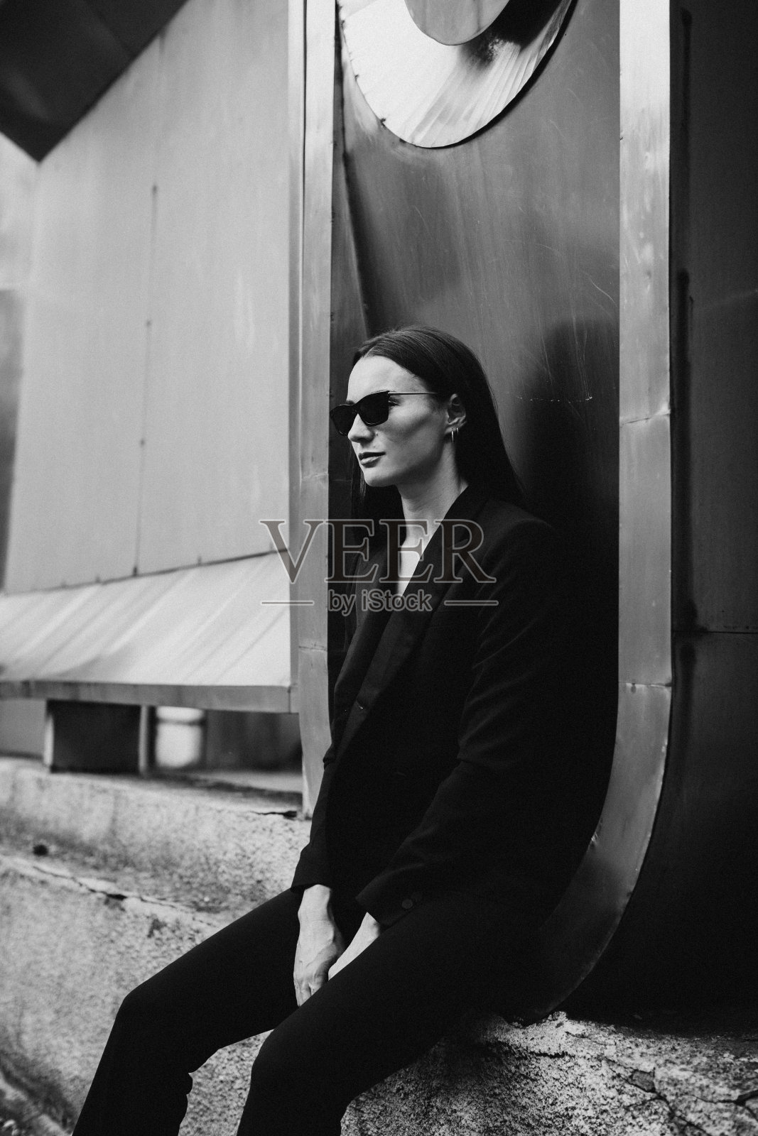 户外年轻优雅女子的时尚肖像。黑色西装，墨镜，灰色金属背景。照片摄影图片