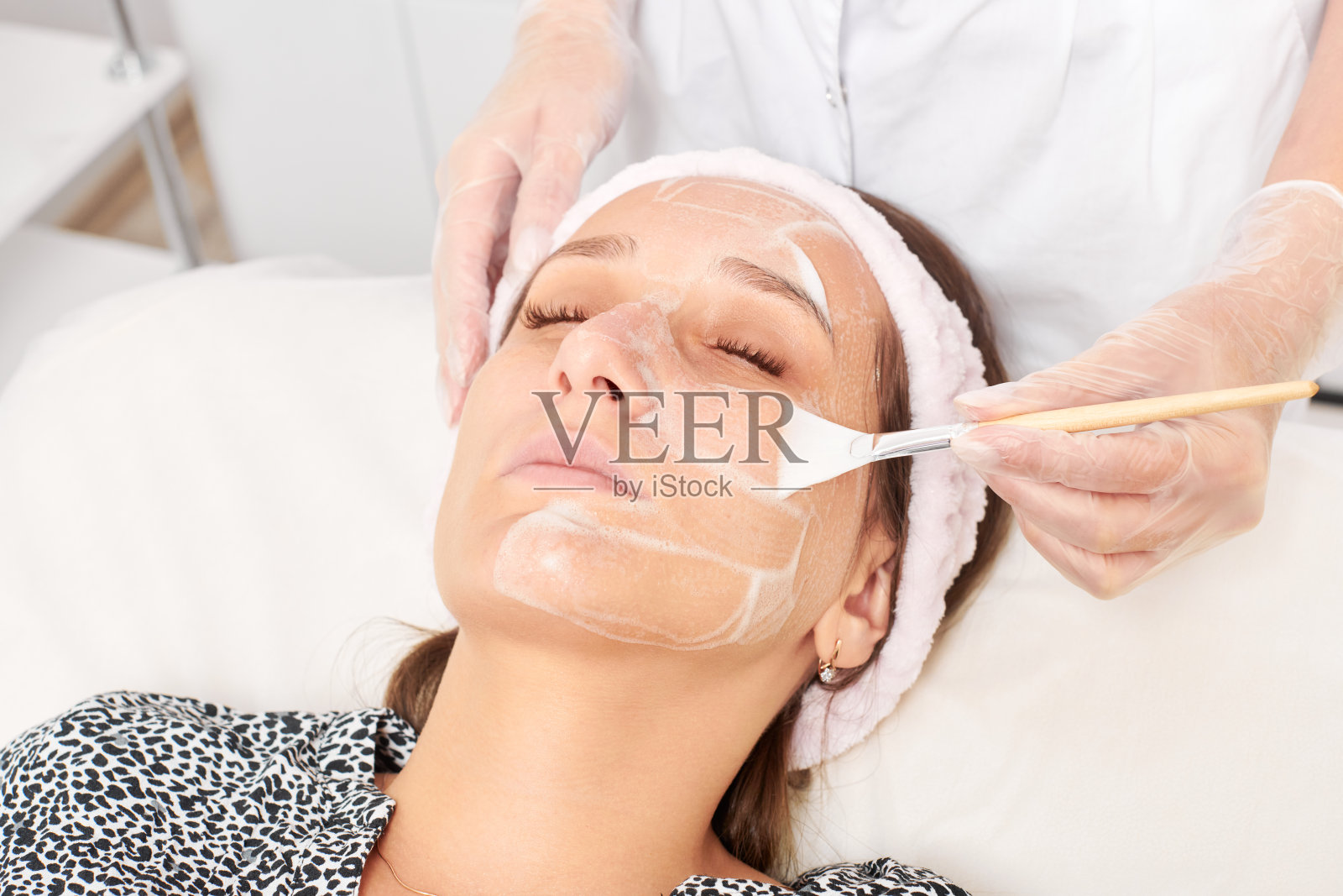 美容院美容师在女性脸上涂抹美容霜面膜，进行年轻化手术照片摄影图片