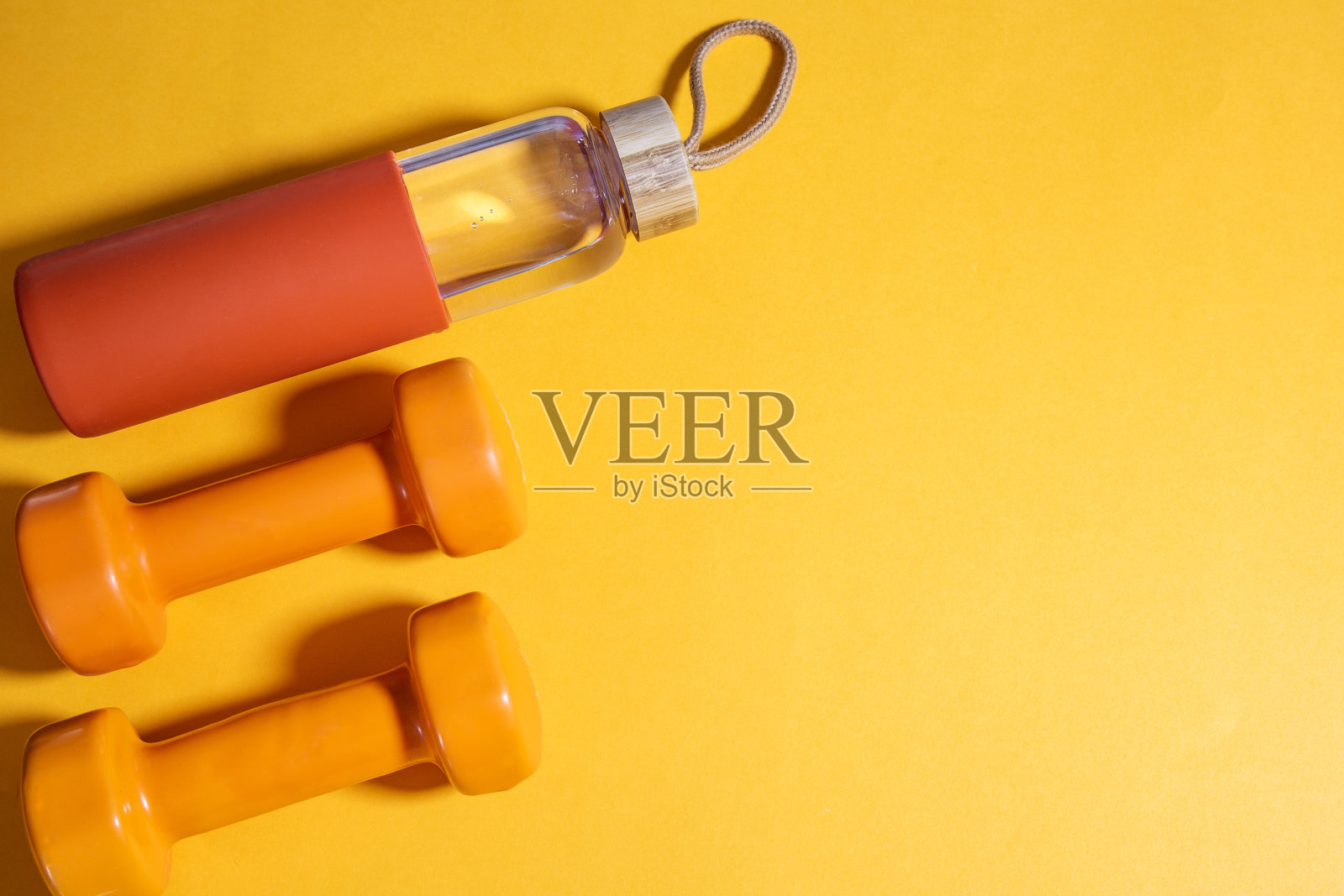 黄色背景上有两个橙色哑铃和水瓶，平铺，留出文字空间照片摄影图片