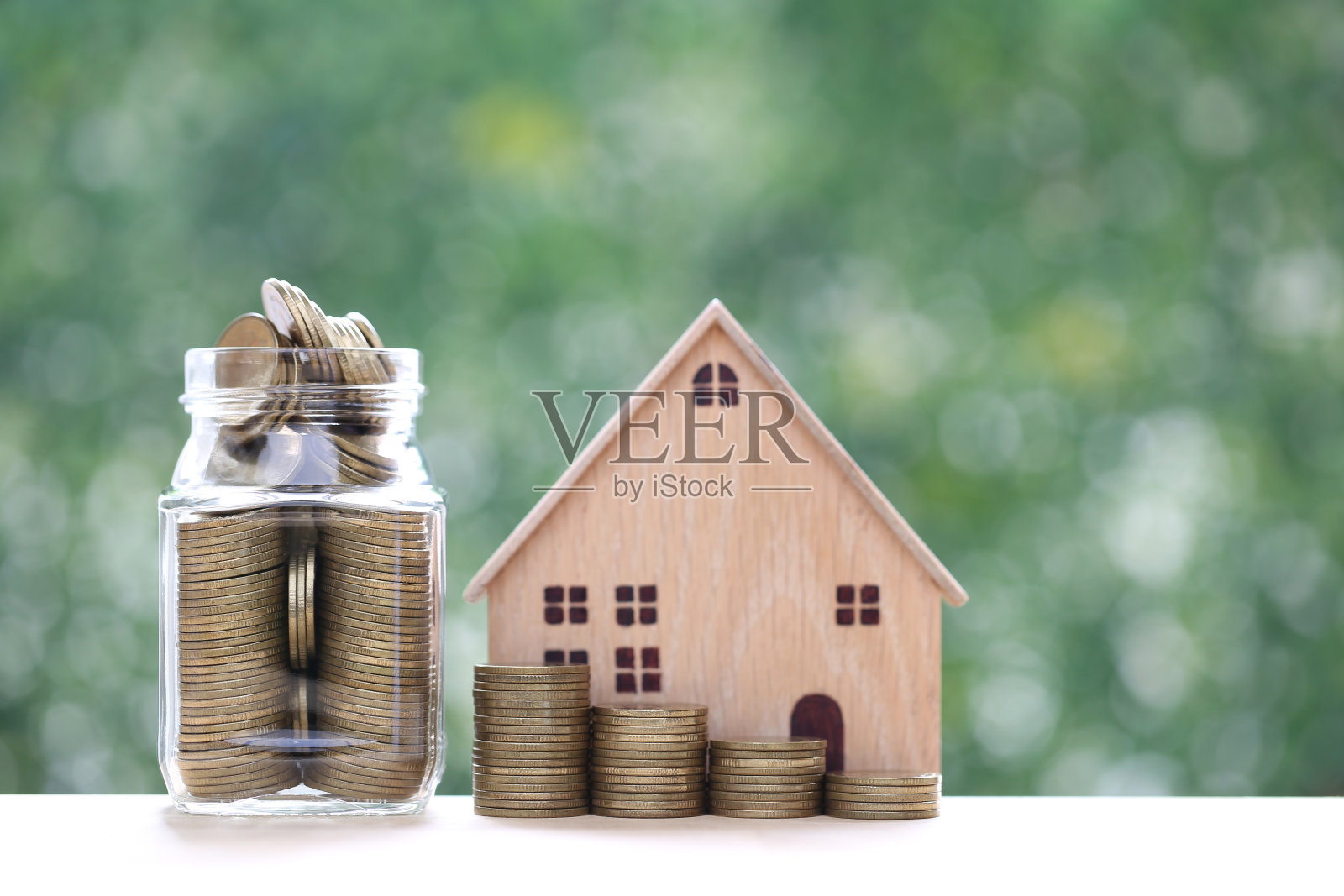 抵押贷款，样板房和一堆硬币在玻璃瓶子上自然绿色背景，商业投资和房地产概念照片摄影图片