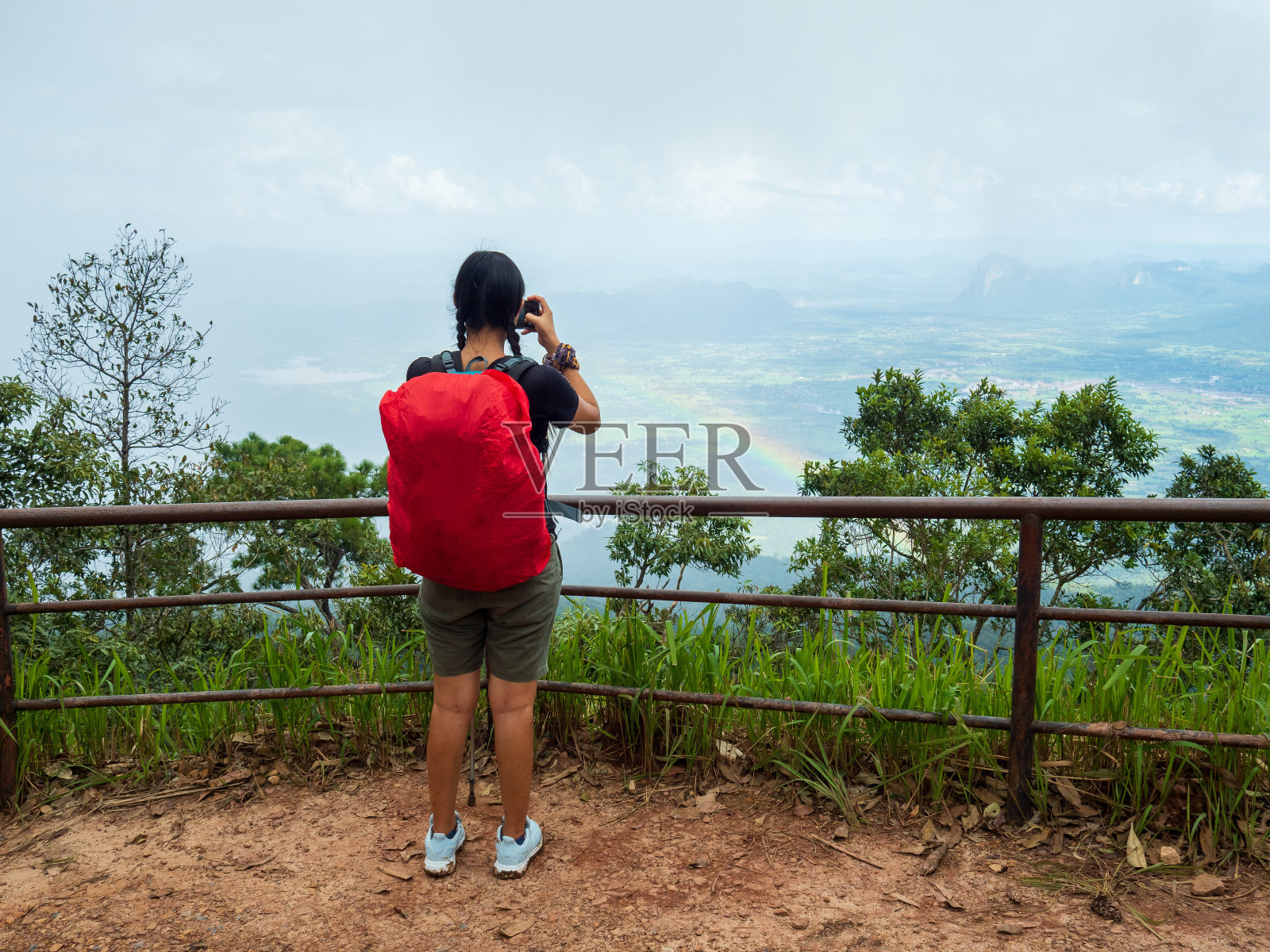 一位背着红色背包的女性徒步旅行者站在那里，用手机记录自然风景。在丰富的森林自然之中照片摄影图片