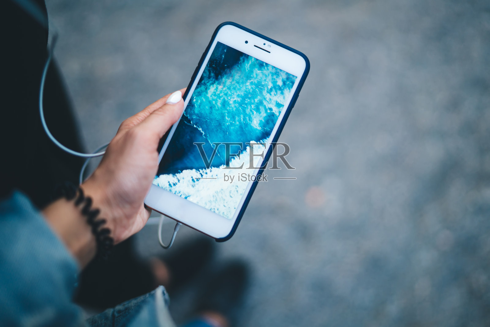 短发女博主使用电子耳机听音乐播客和现代智能手机设备显示屏保，女孩手持数字蜂窝设备与海洋图像照片摄影图片