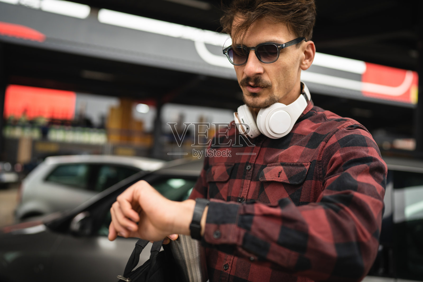 一名年轻男子站在停车场查看手表上的时间照片摄影图片