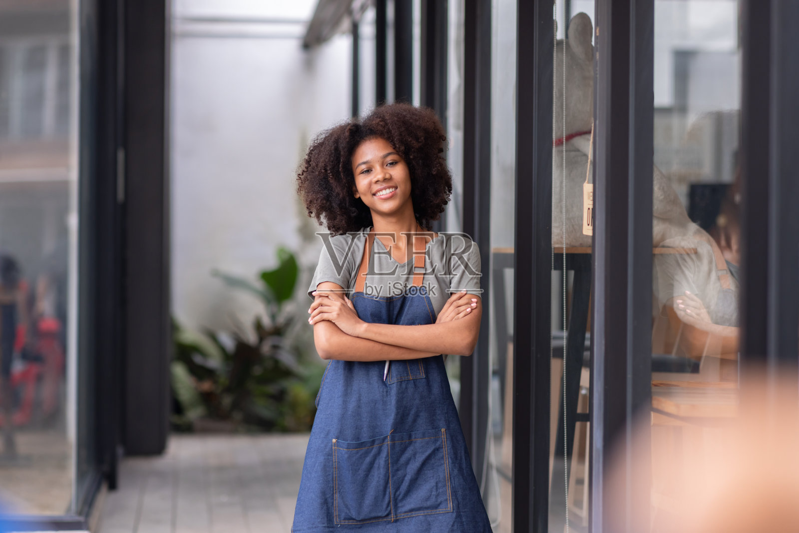 一名非洲小商人是一名围着围裙的女服务员，咖啡馆的老板站在门口，举着“开门”的牌子等待顾客。小型商业概念，咖啡馆和餐厅照片摄影图片