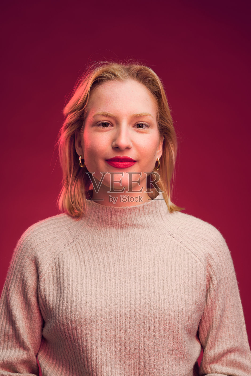 一个快乐的女人在工作室摆姿势，微笑在相机孤立在洋红色背景的肖像。洋红色万岁，年度流行色。照片摄影图片