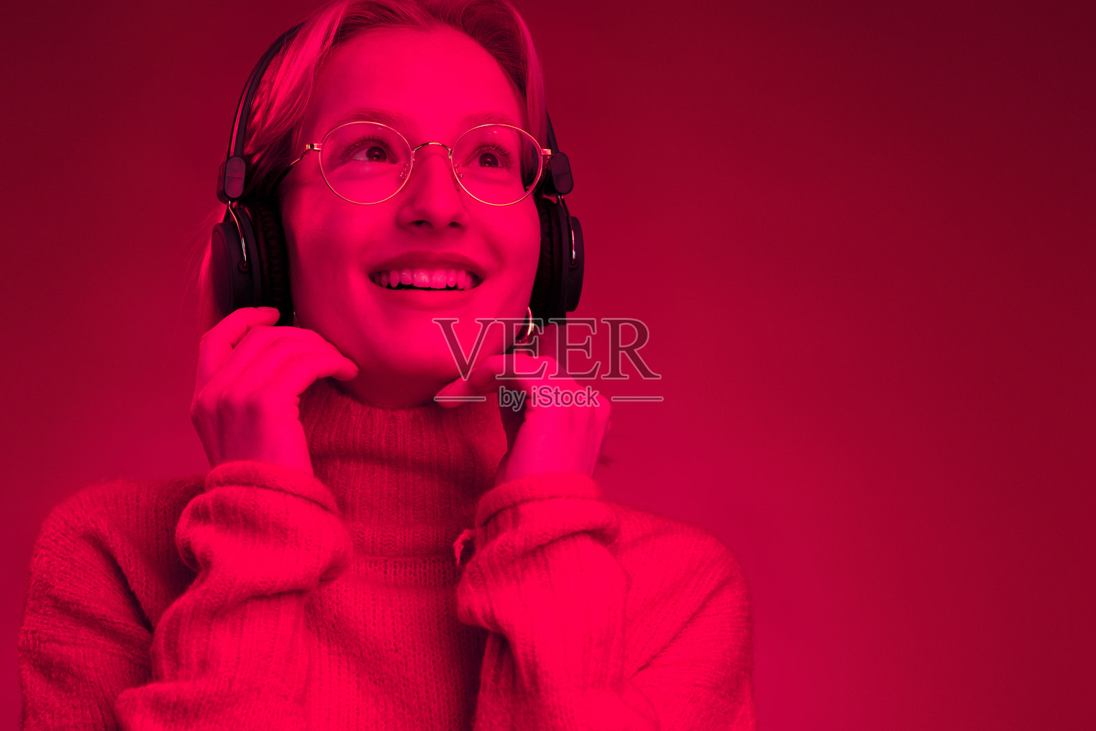 一个女孩在品红背景上享受音乐的单色图片。洋红色万岁，年度流行色。照片摄影图片