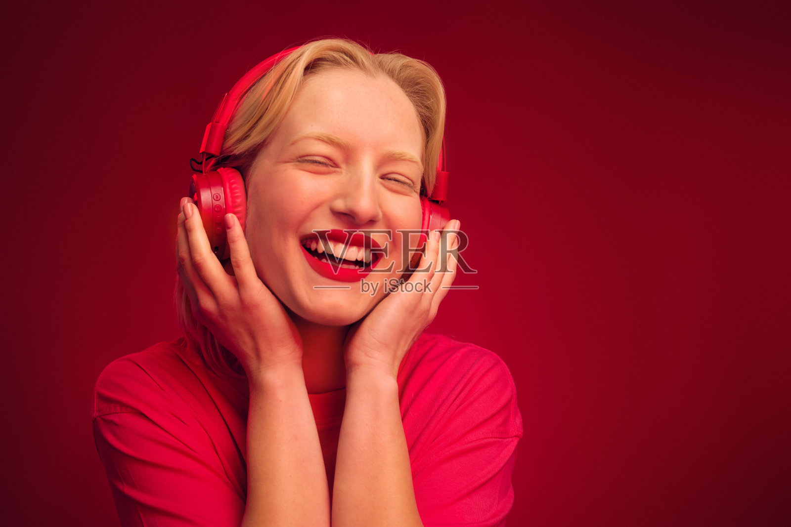 一位快乐的年轻女子独自站在紫红色的背景上，一边跳舞一边欣赏音乐。洋红色万岁。照片摄影图片