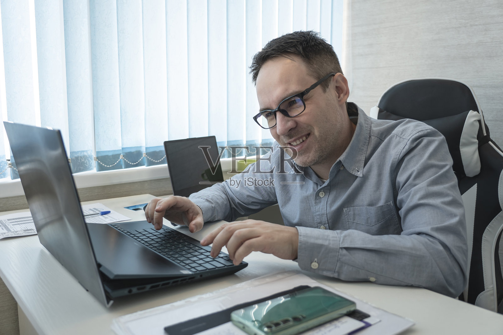 一位身穿蓝色衬衫、戴着眼镜的年轻职员在办公室微笑。优雅的商人在办公室分析数据照片摄影图片