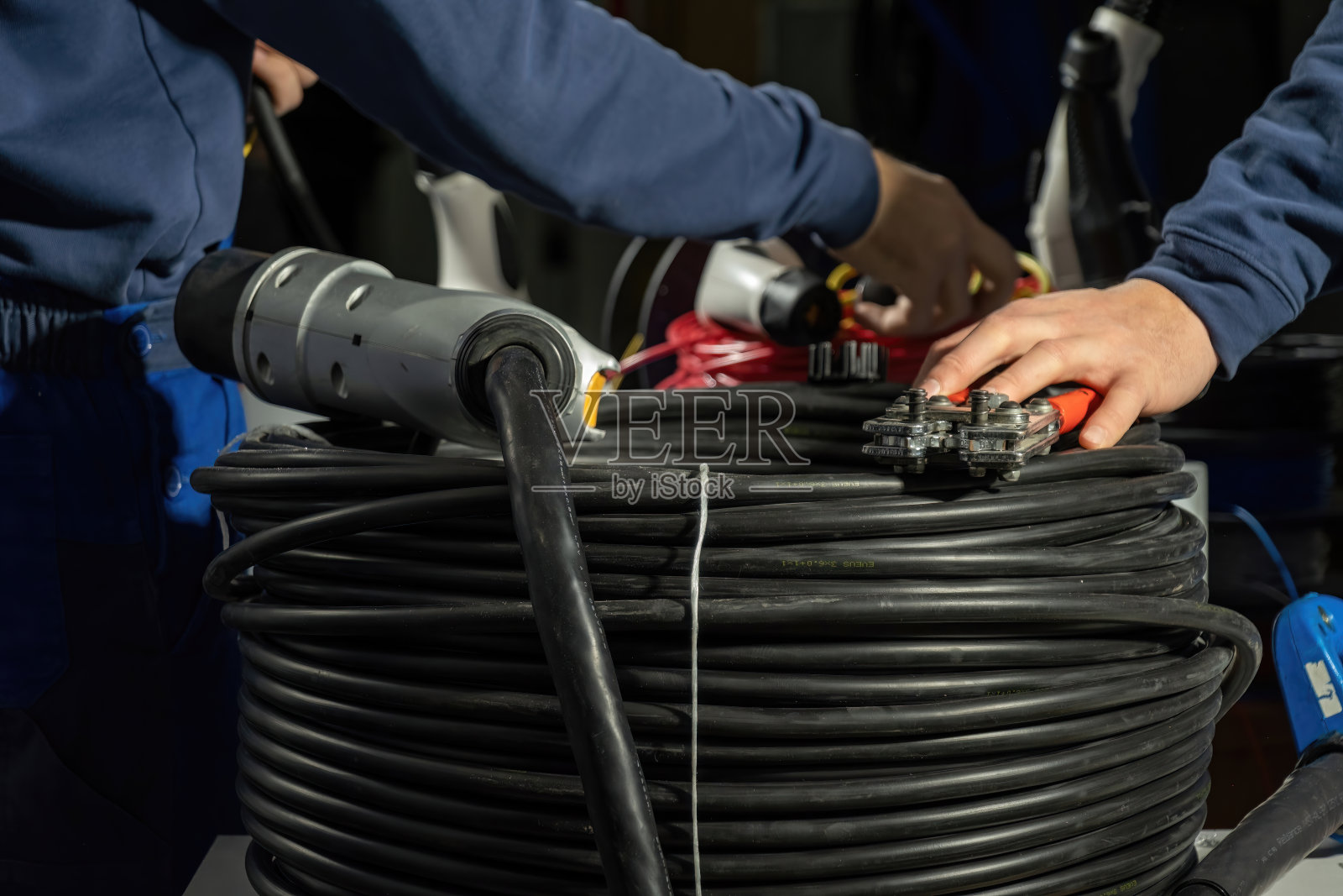 电工将电缆安装在插头上，为电站的电动汽车充电照片摄影图片