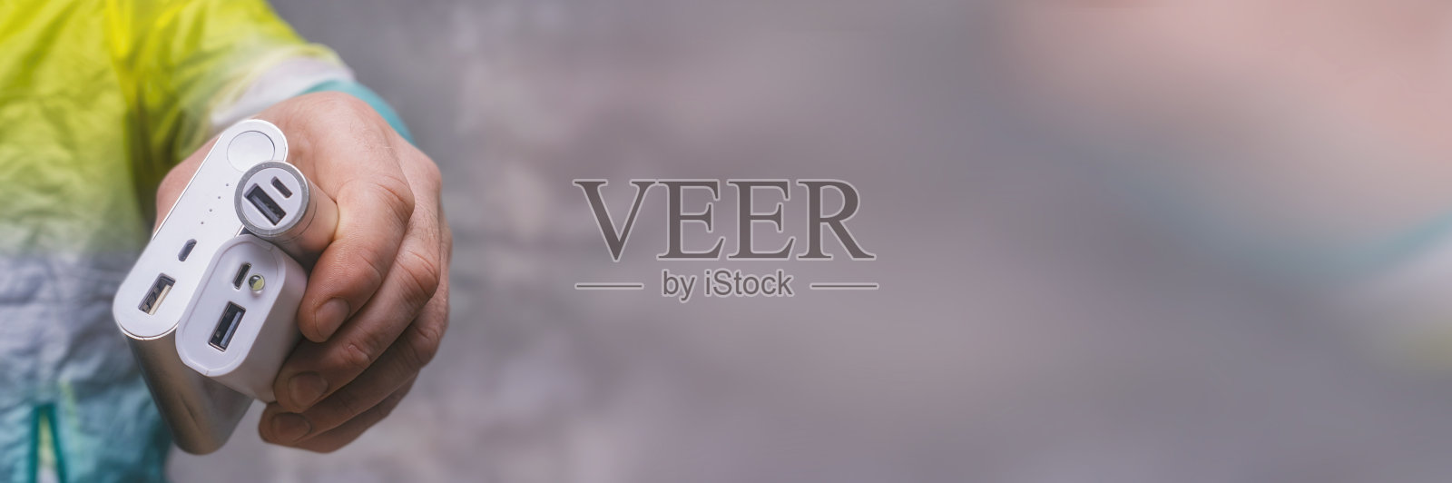 一男子手里拿着充电宝，对着混凝土墙给智能手机充电。照片摄影图片