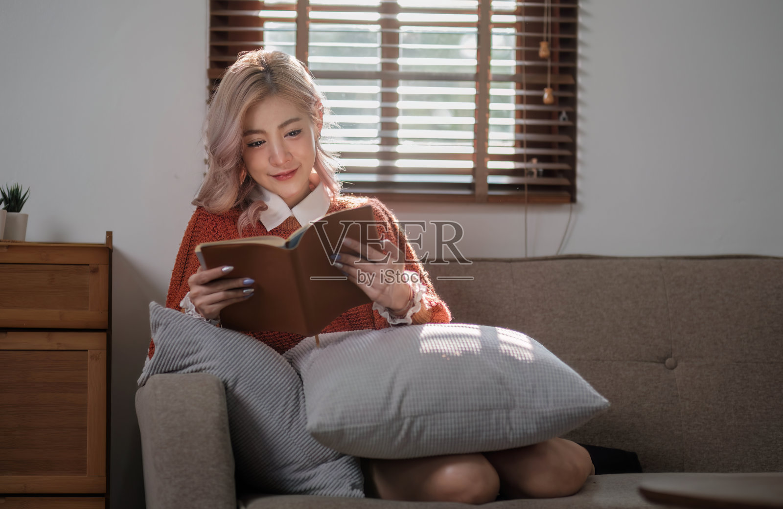 迷人的年轻亚洲女子坐在最小和舒适的客厅享受读书。照片摄影图片