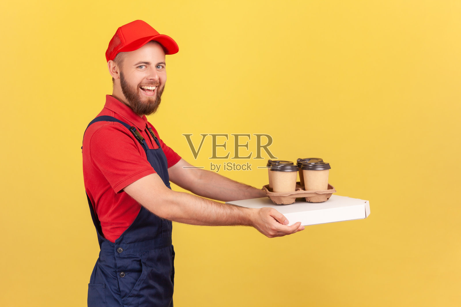 送餐员拿着披萨盒和一次性杯子里的咖啡站在那里，微笑着看着镜头。照片摄影图片