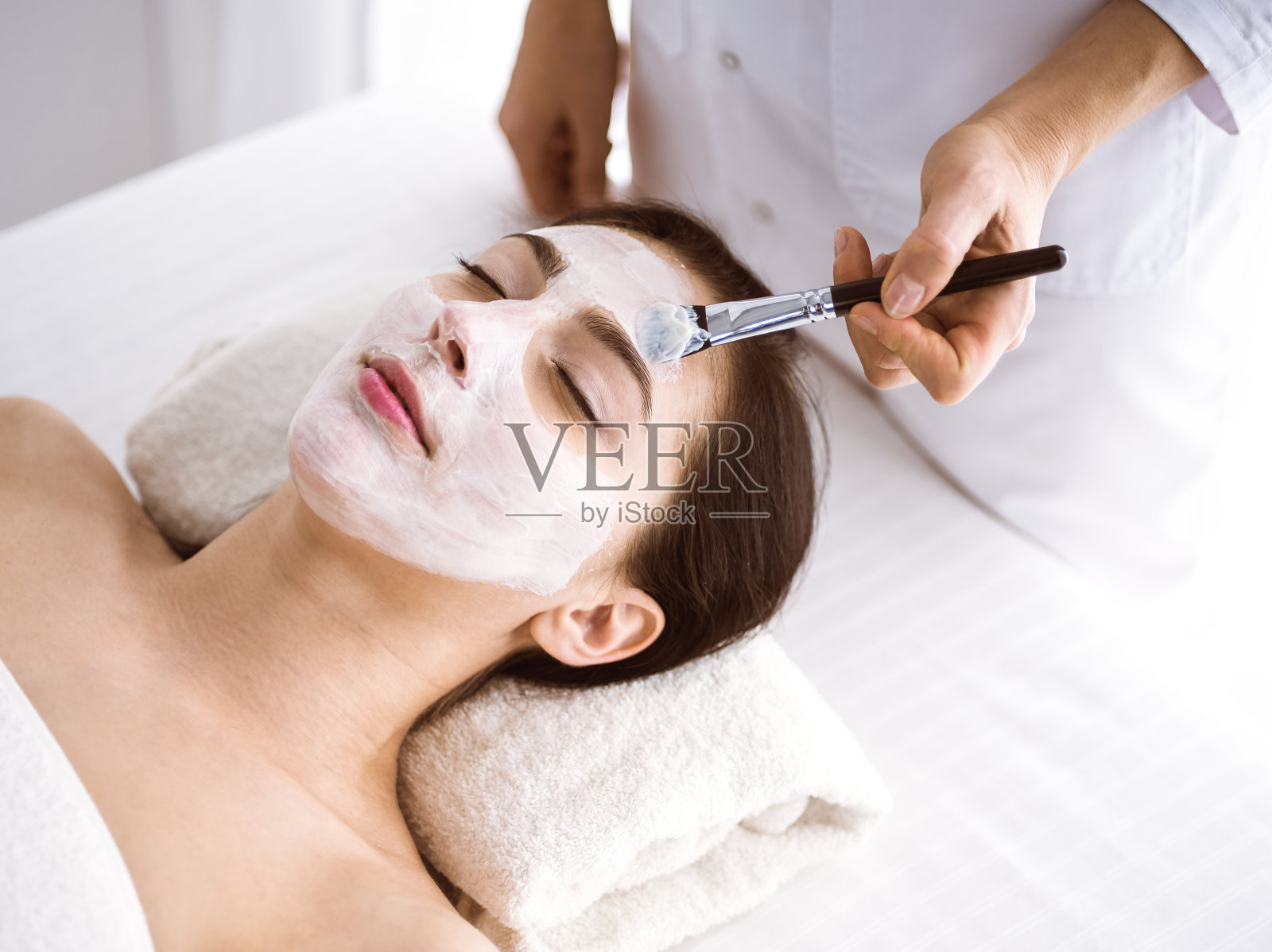 美丽的黑发女子享受使用美容面膜舒适和bis丰满。放松治疗在医学和水疗中心的概念照片摄影图片