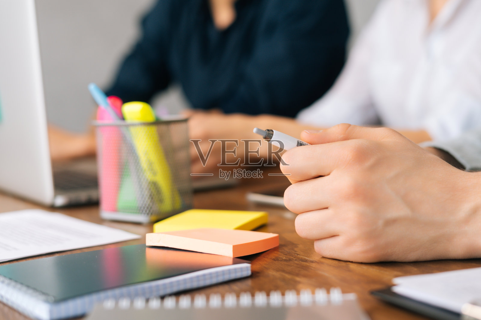 在交易会议期间，难以辨认的商人坐在桌子旁握着笔。企业决策。照片摄影图片