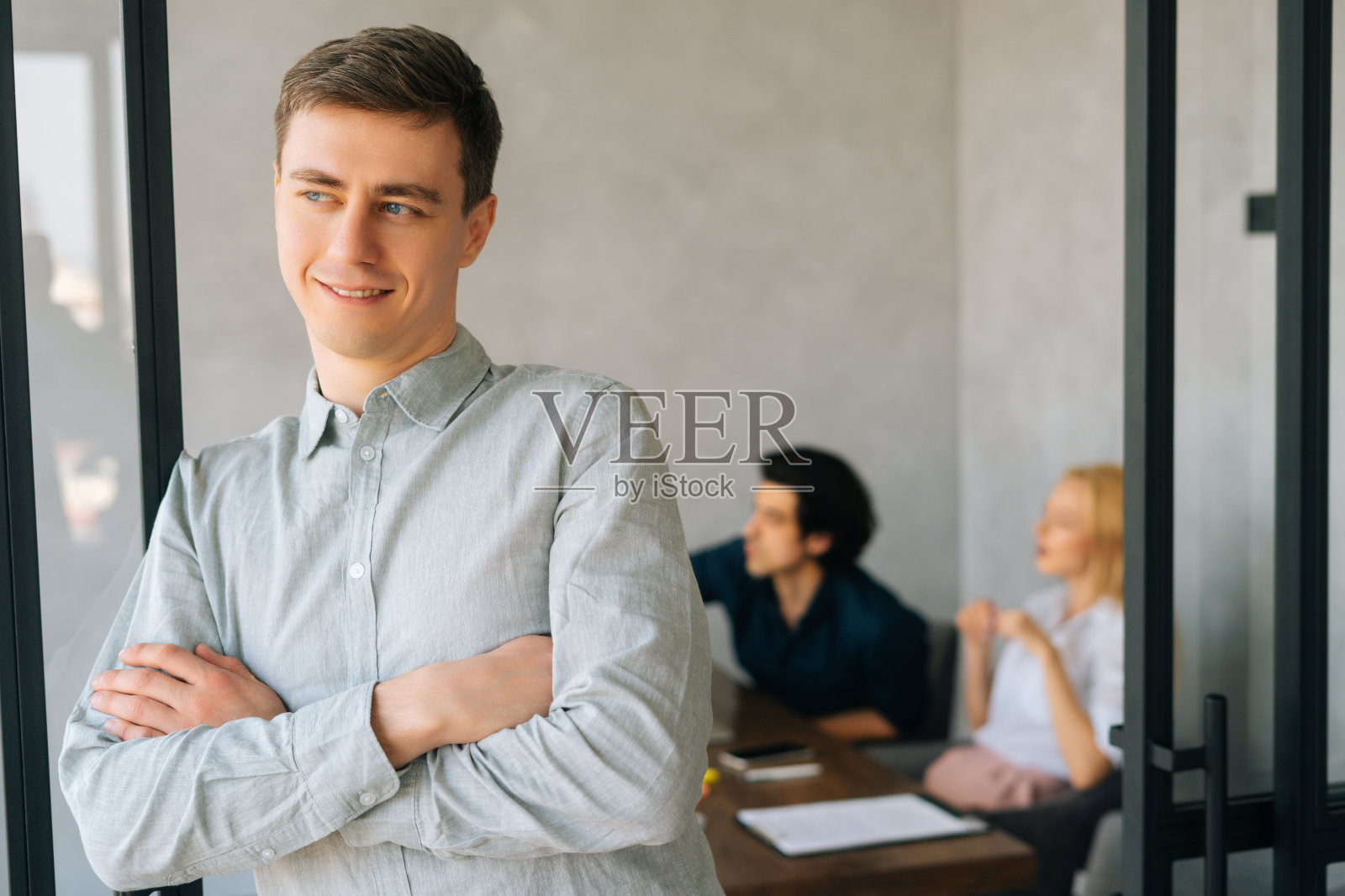 英俊自信的年轻商人在休闲装站在办公室微笑着看向别处。商务团队讨论项目照片摄影图片