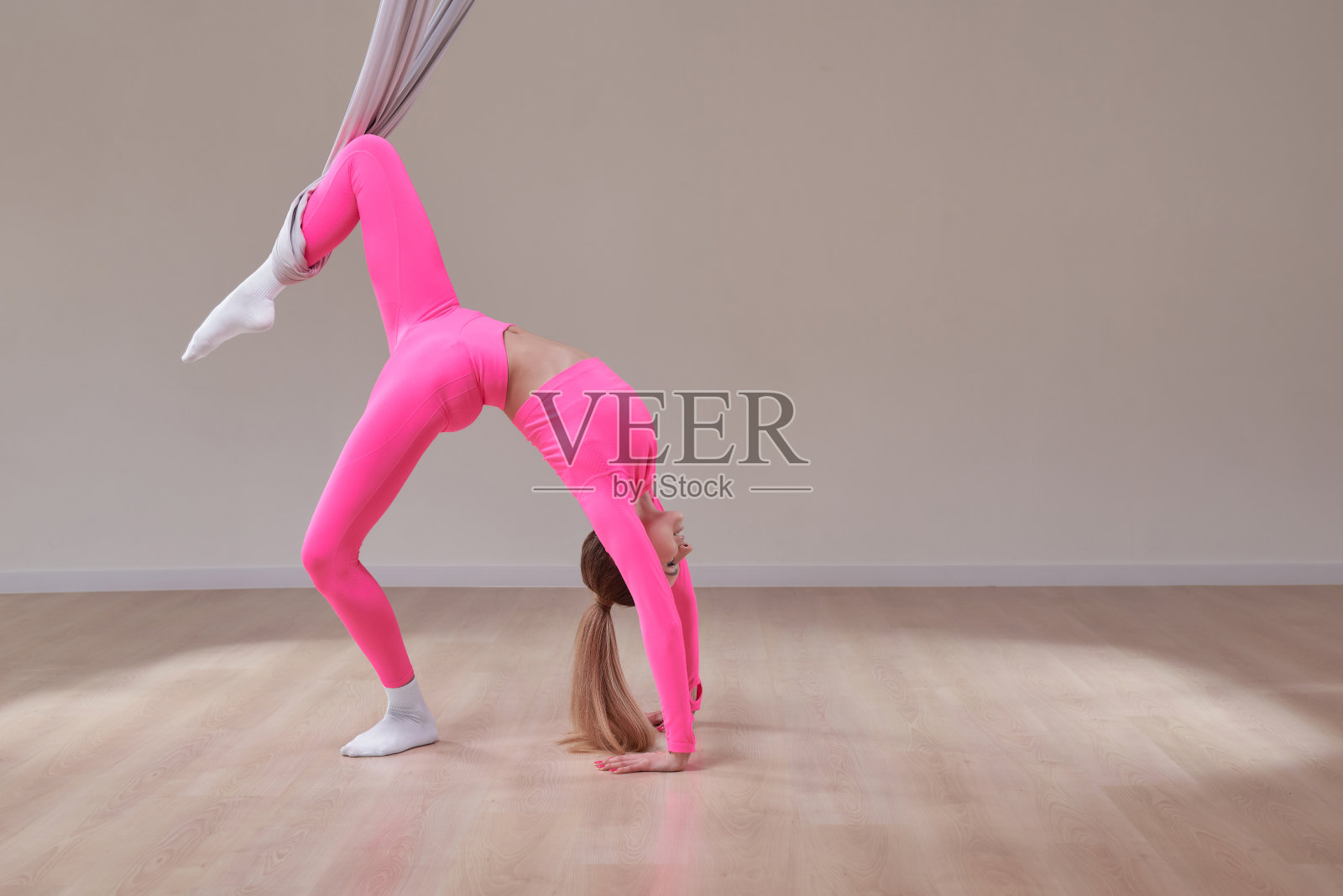 美丽的运动女孩在粉红色的制服做反重力瑜伽和空气拉伸姿势。健康生活方式的概念。照片摄影图片