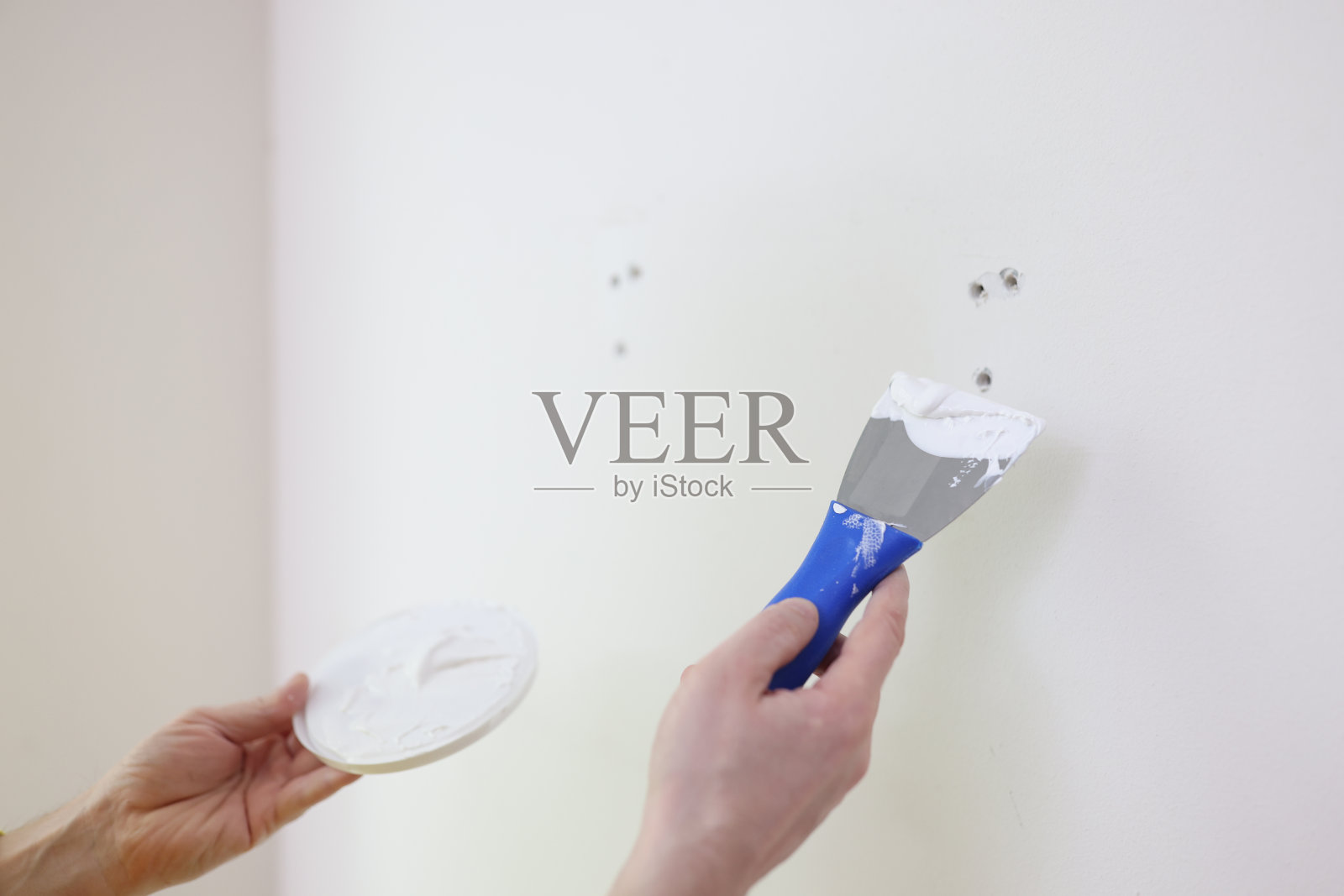 建筑工或修理工用油灰刀抹灰白墙的近景。照片摄影图片