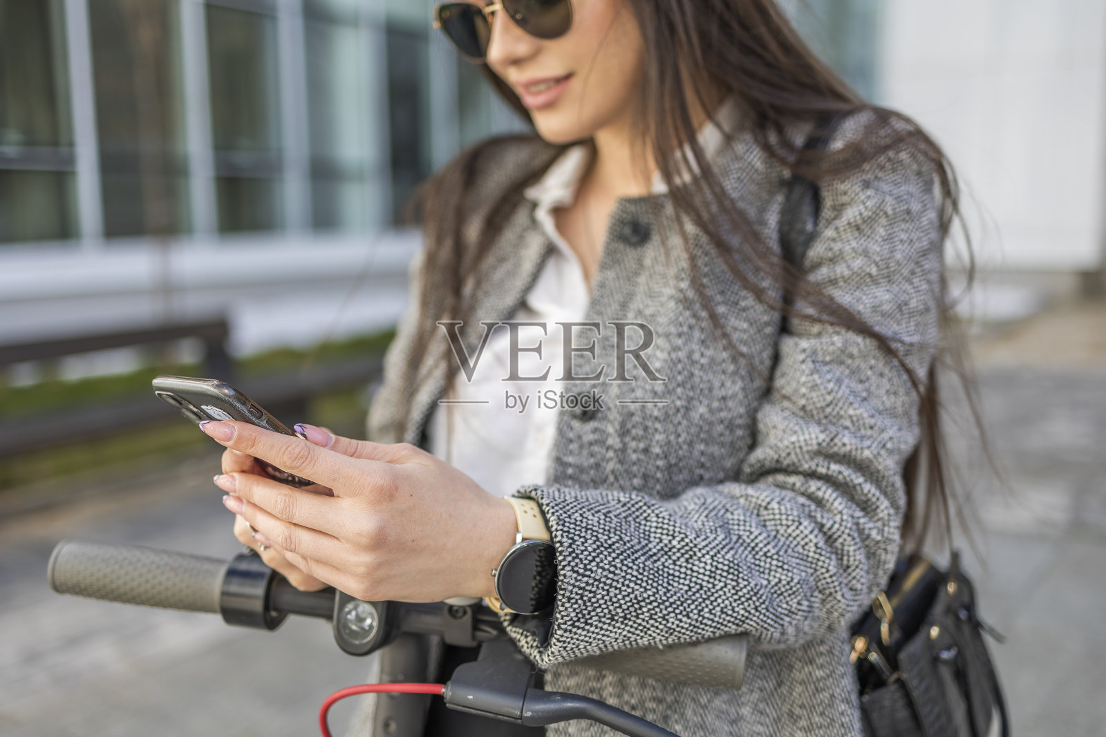 一位现代商业女性一边打电话一边骑着电动滑板车来上班。照片摄影图片