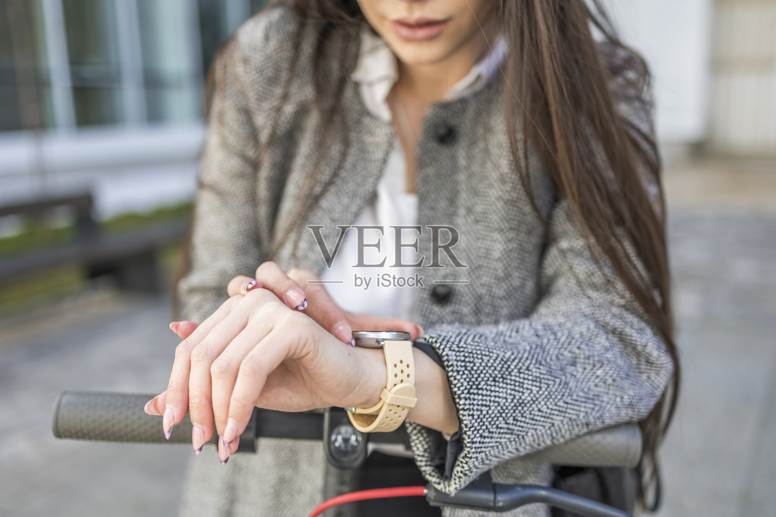 一名女商人在骑电动滑板车时查看智能手表上的时间。照片摄影图片