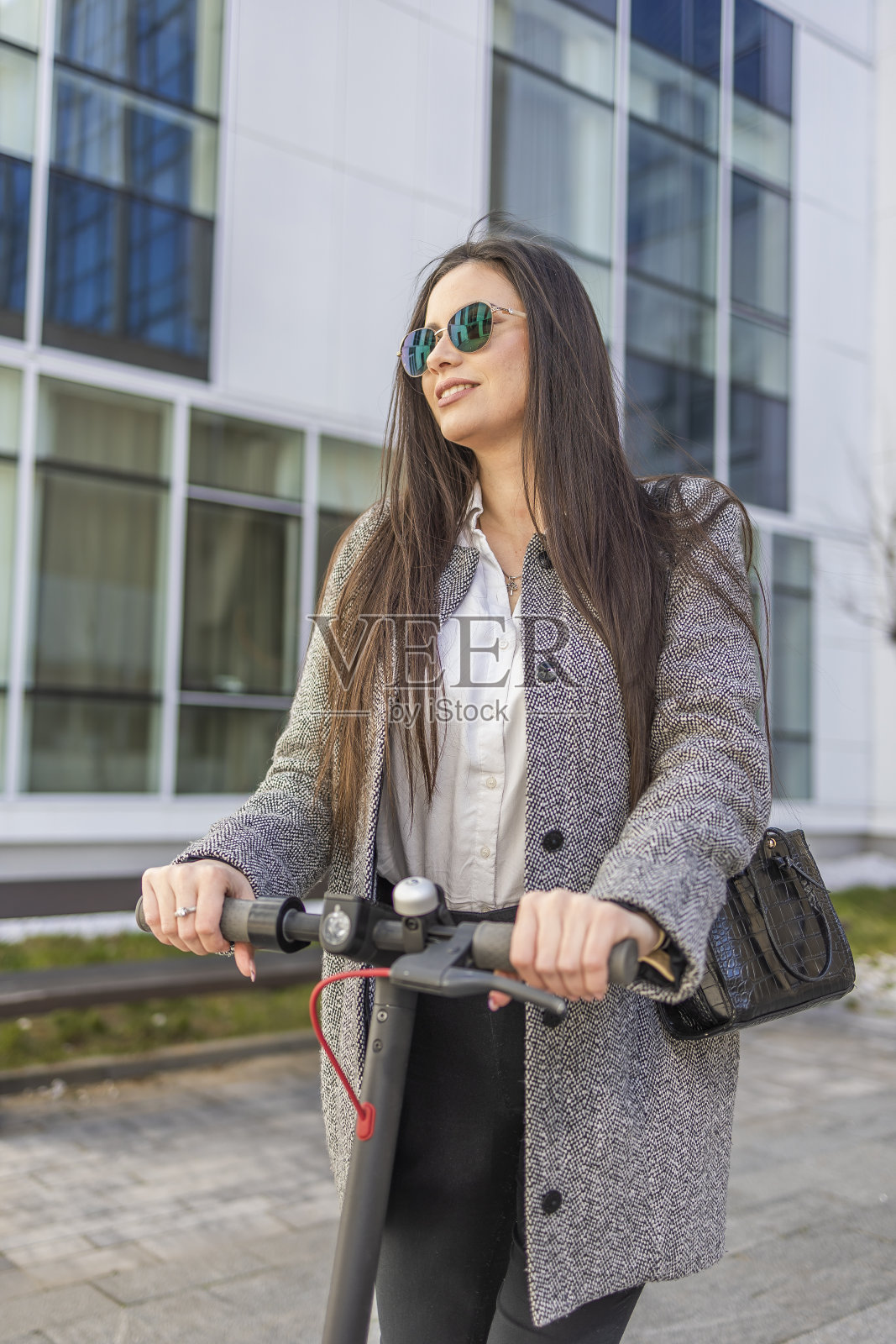 每小时更多的微笑。一个时尚的女孩微笑着沿着城市骑电动滑板车的肖像。照片摄影图片