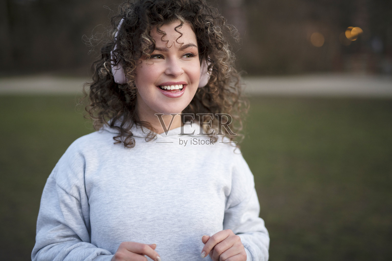年轻漂亮的女人穿着灰色运动帽衫，戴着耳机，晚上在公园里听音乐照片摄影图片