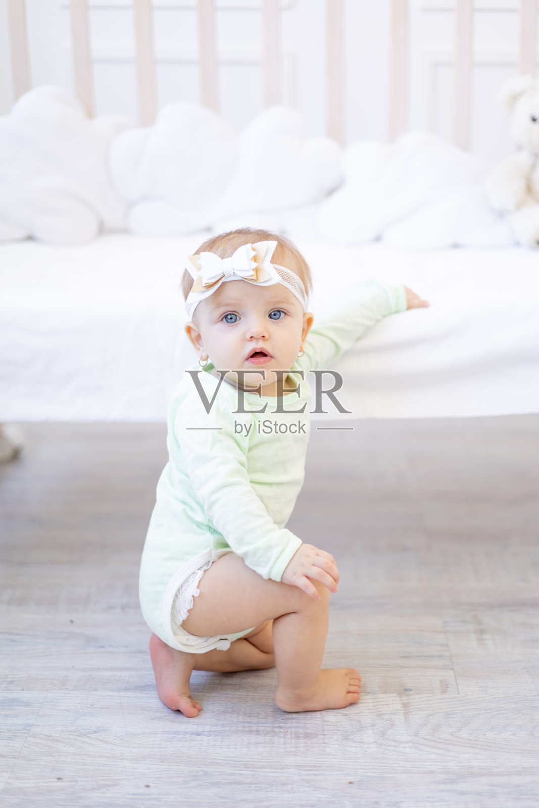 一个穿着白色棉质紧身衣的小女婴站在或爬在托儿所的婴儿床上，她正在学习走路照片摄影图片