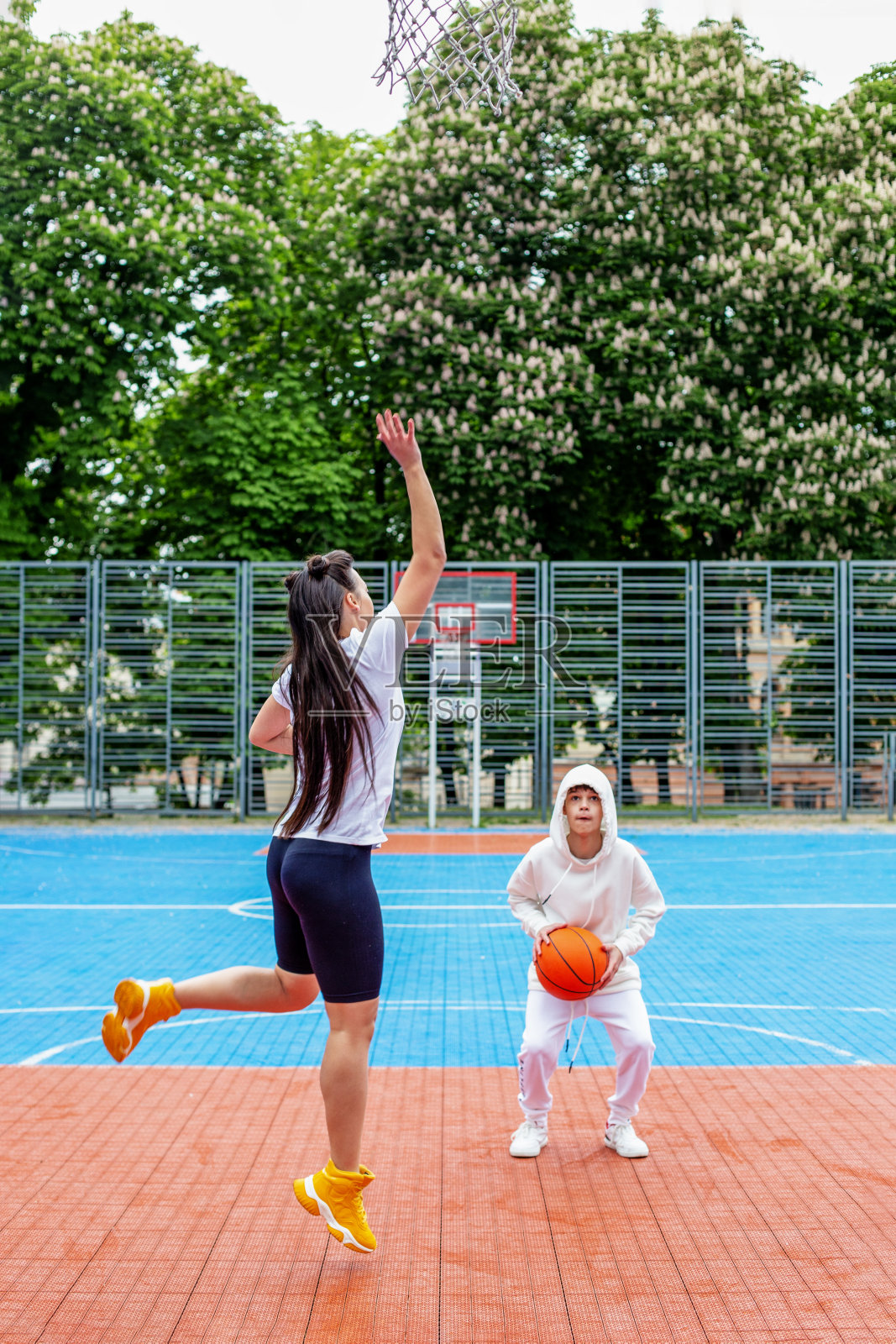 女孩和十几岁的弟弟在露天的现代篮球场上打篮球照片摄影图片