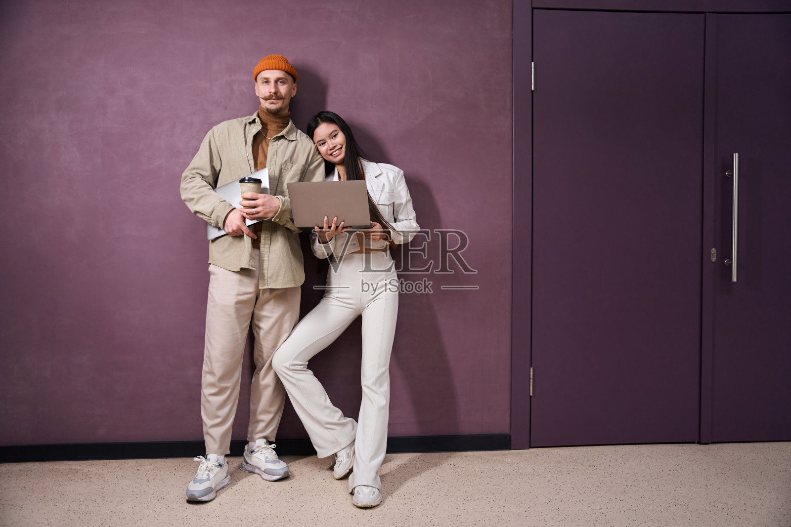 一对年轻夫妇拿着笔记本电脑站在墙边照片摄影图片