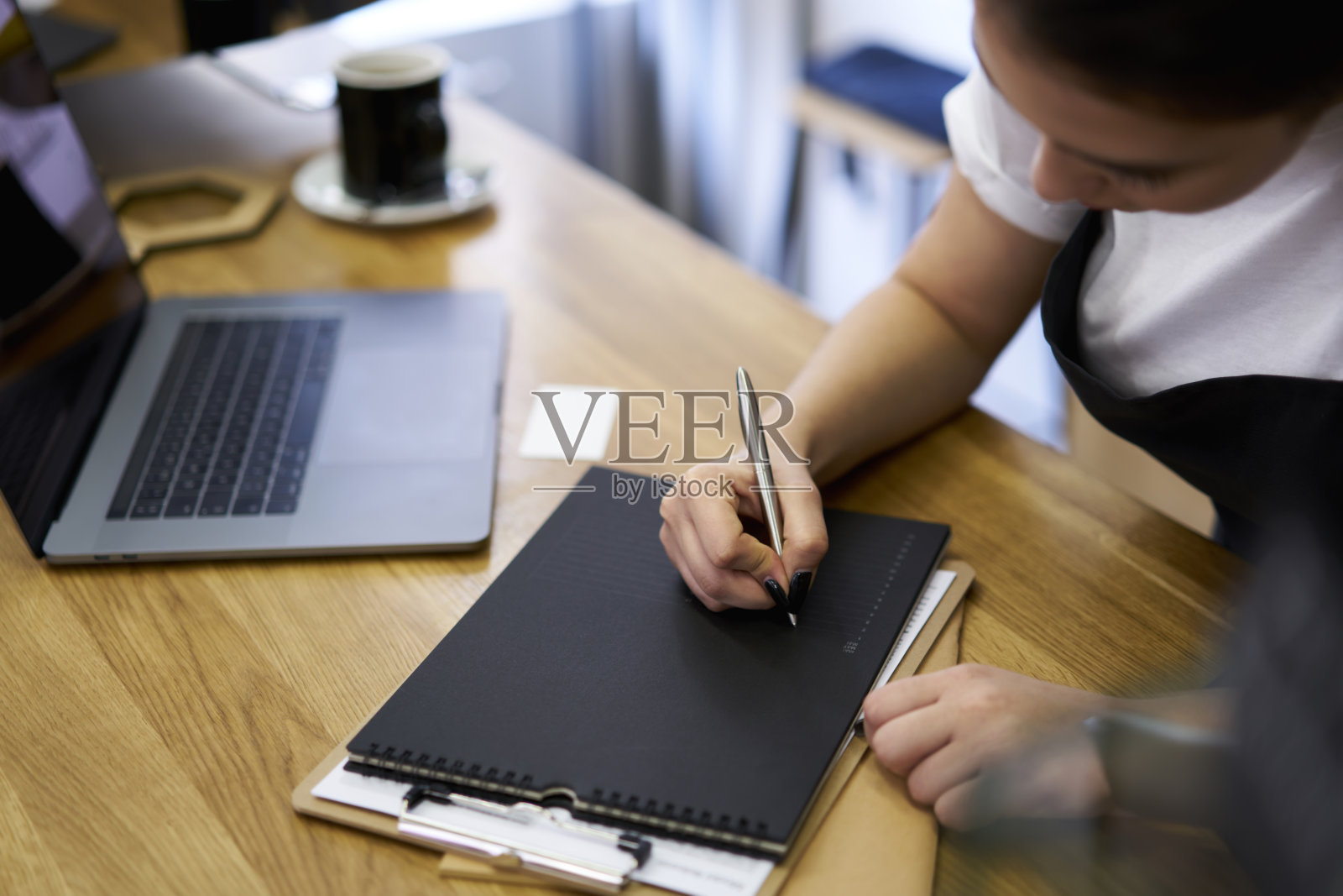 裁剪图像熟练的女服务员在咖啡店的工作场所写关于零售和预算账单的报告，年轻女子在笔记本电脑附近用笔填写就业写作表格照片摄影图片