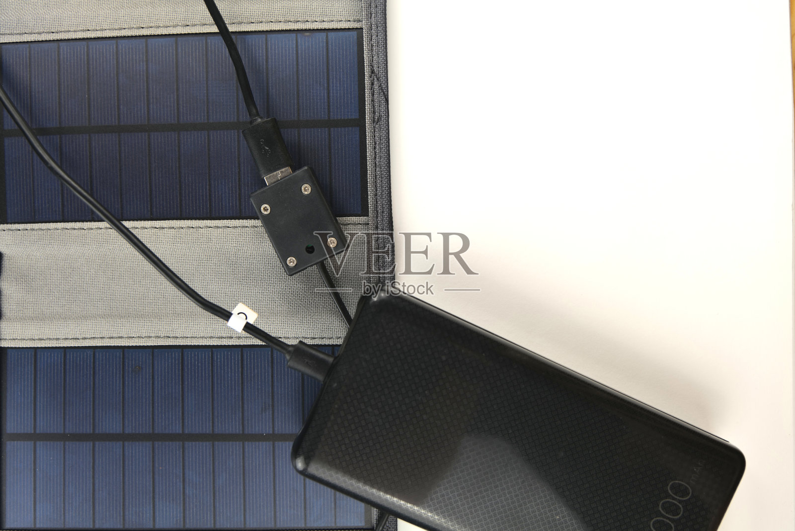 一个巨大的黑色充电宝正在用白色背景的便携式太阳能板充电照片摄影图片