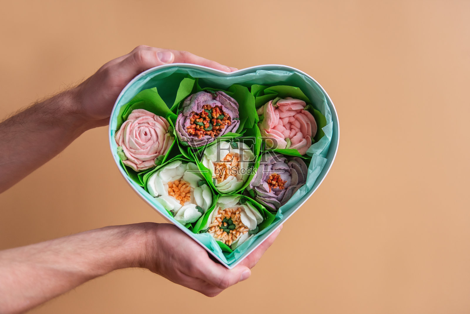 在橙色孤立的背景下，男性手握心形礼盒与甜蜜的棉花糖花。照片摄影图片