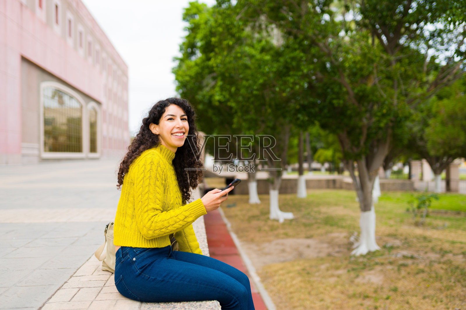 漂亮的女人在户外放松，同时在她的智能手机上发短信照片摄影图片