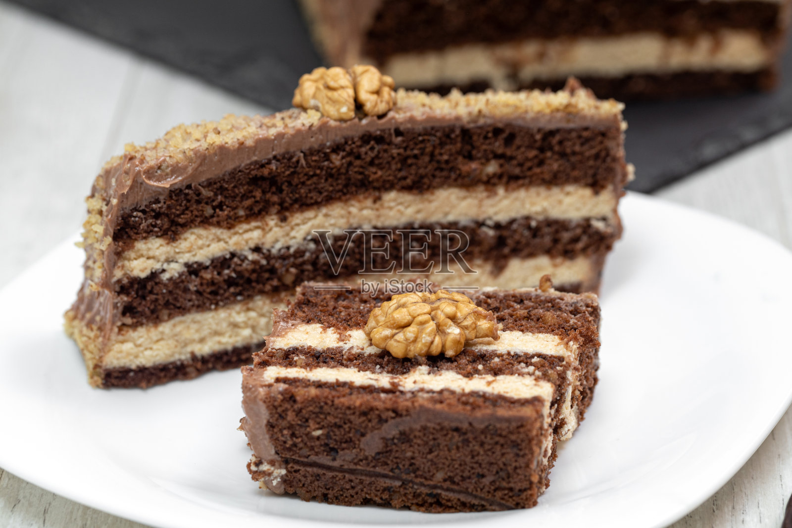 甜坚果甜点，巧克力泡芙蛋糕，一块奶油蛋糕放在白色的盘子里，还有坚果照片摄影图片