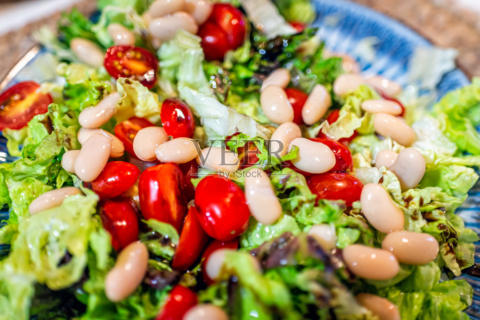 切碎的彩色蔬菜作为新鲜的素食沙拉，红叶生菜和红樱桃葡萄西红柿和白豆放在蓝色的盘子里照片摄影图片