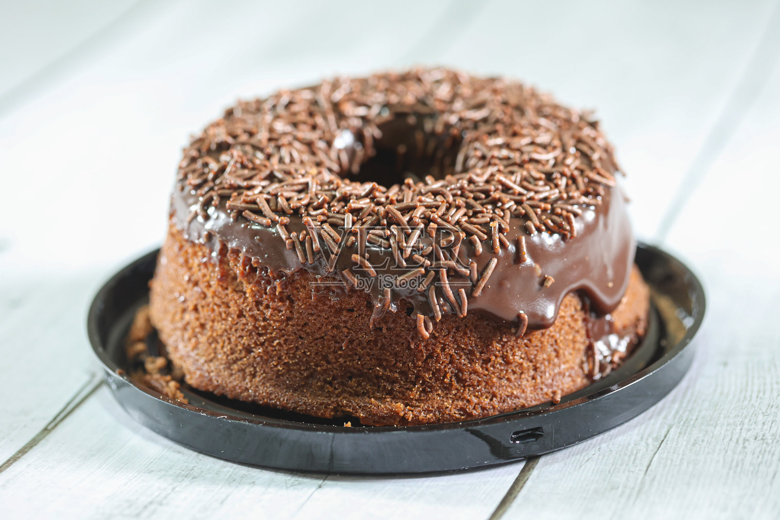 一种巧克力蛋糕，上面有巧克力糖霜和巧克力粉装饰。在巴西，它被称为bolo de brigadeiro。木制的桌子。照片摄影图片