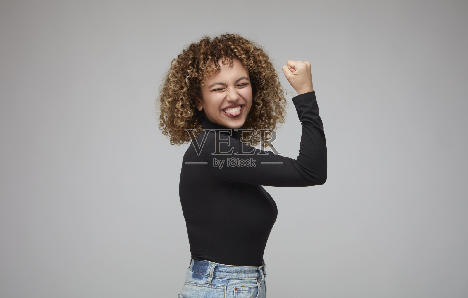 侧身站立，抬起手臂展示肱二头肌的卷发年轻女人照片摄影图片