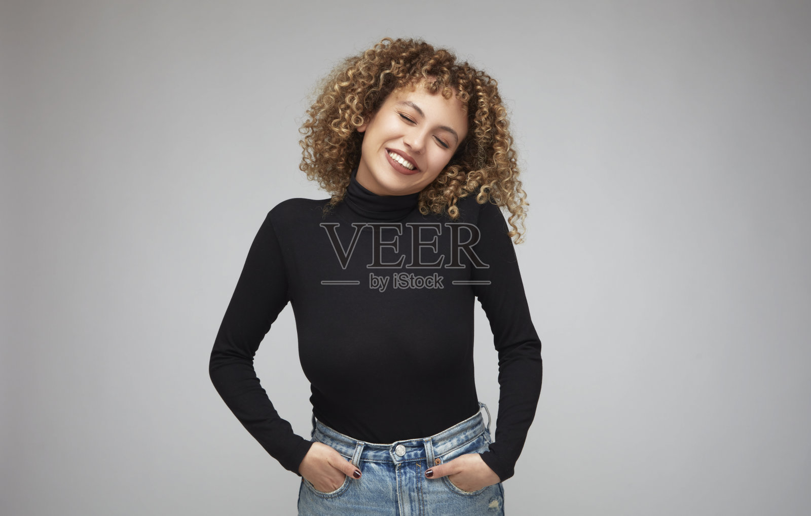 一头卷发的年轻女子闭着眼睛，双手插在口袋里做着白日梦。照片摄影图片