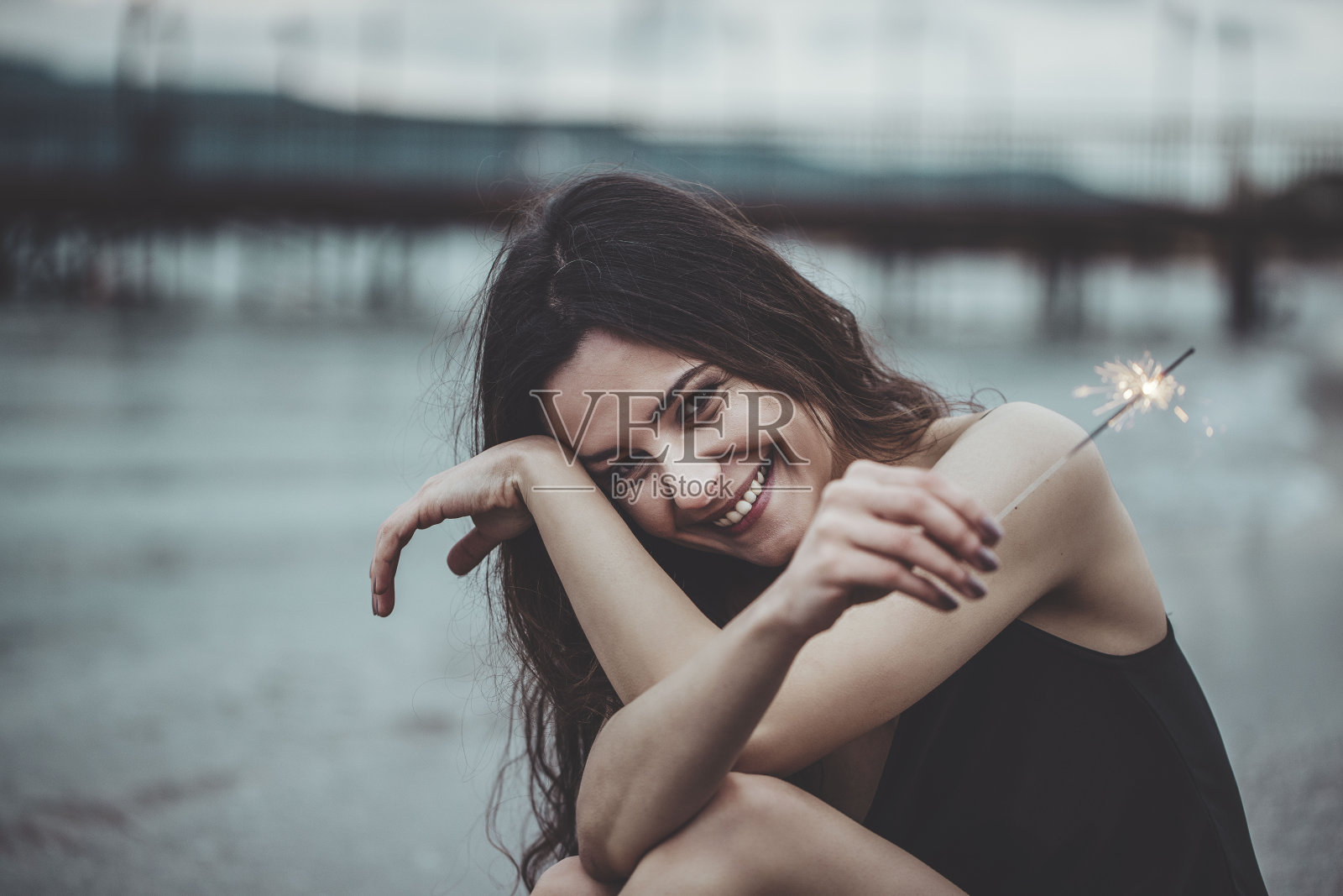 美丽的女人手里拿着烟火正坐在海滩上照片摄影图片