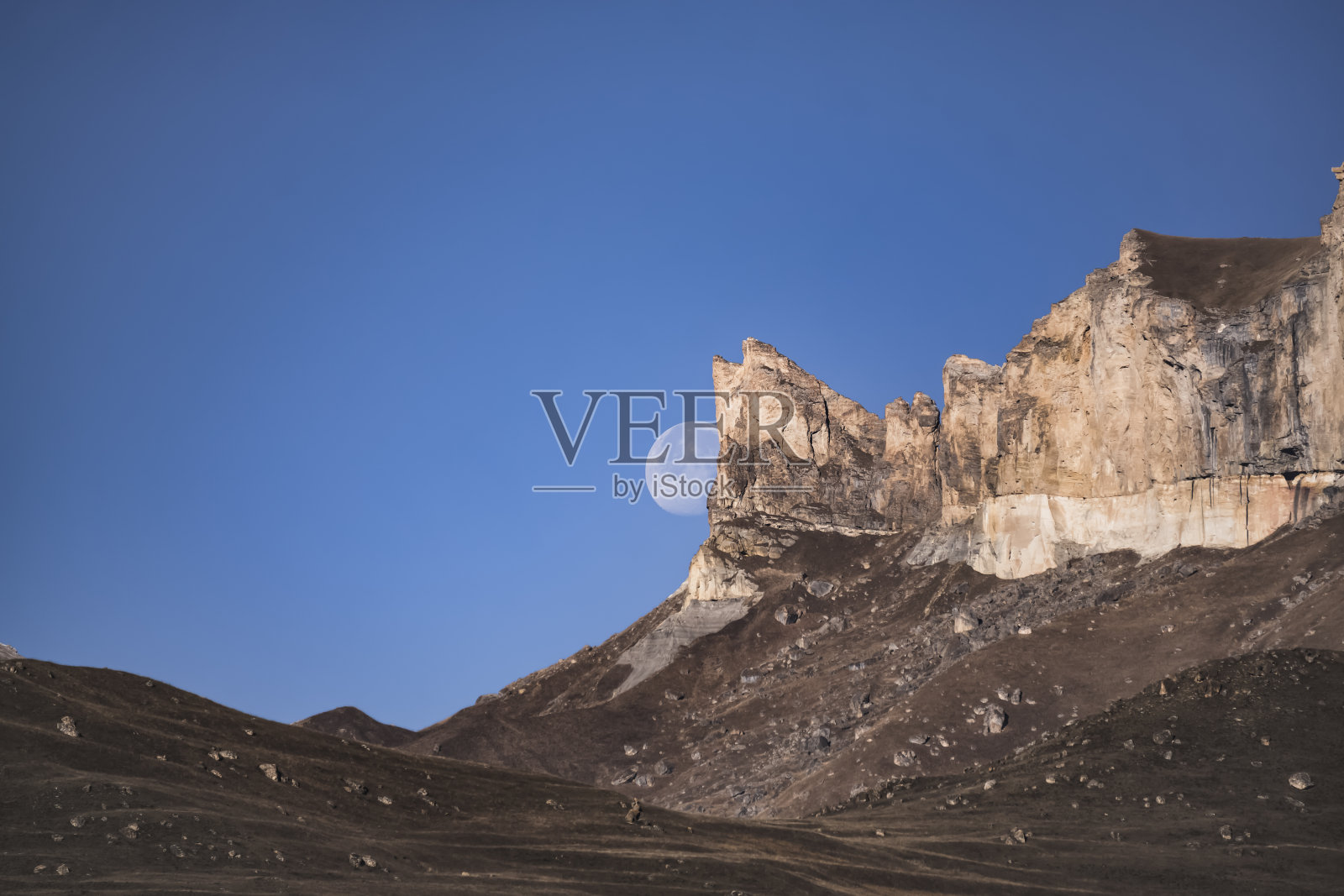 山上的悬崖峭壁在月亮和蓝色的早晨天空的背景下拔地而起，月亮在秋天的山上照片摄影图片