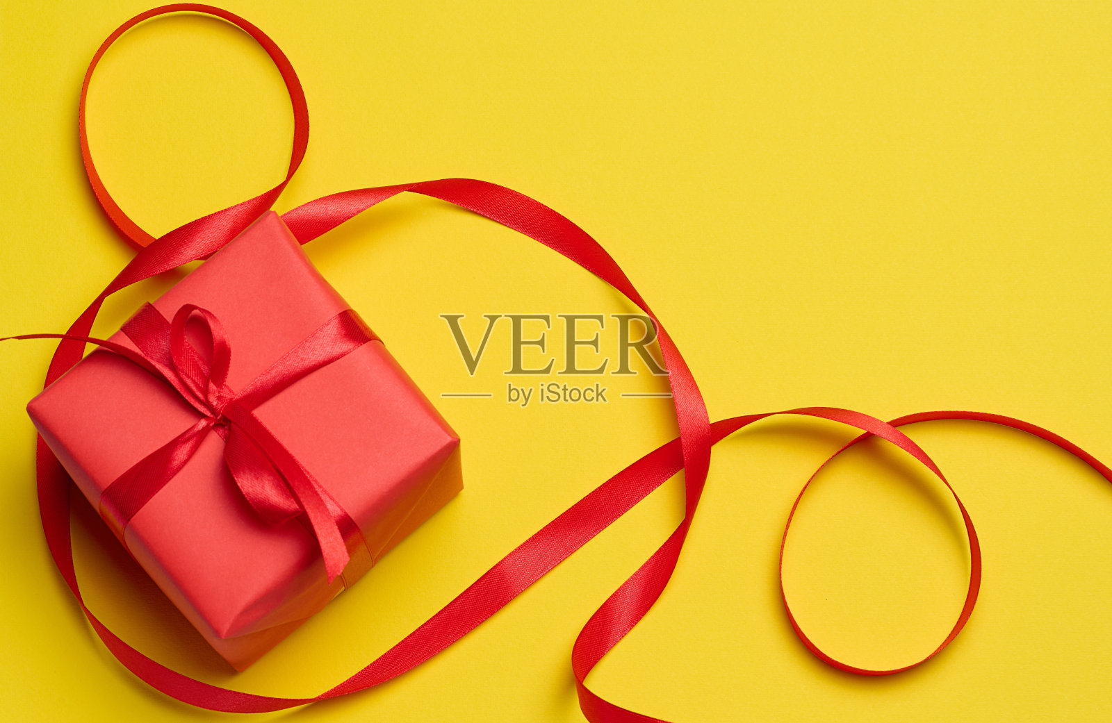 方形盒子系着红色蝴蝶结，黄色背景，俯视图照片摄影图片