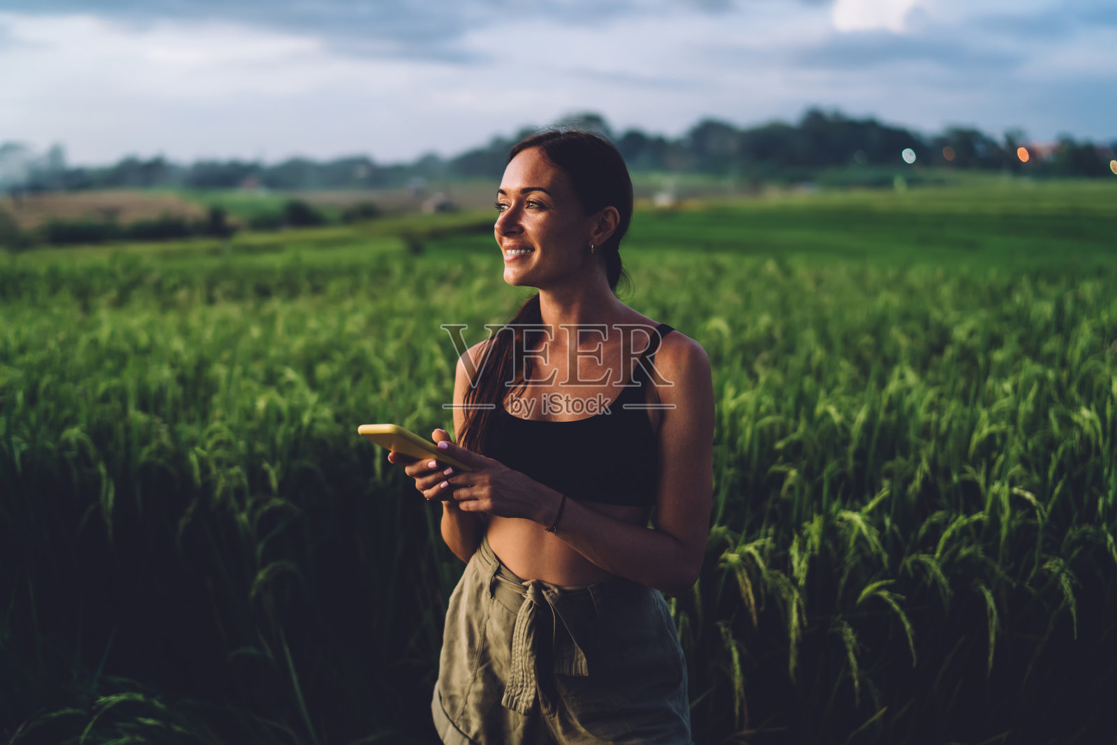 美丽的运动女人拿着智能手机站在田野照片摄影图片