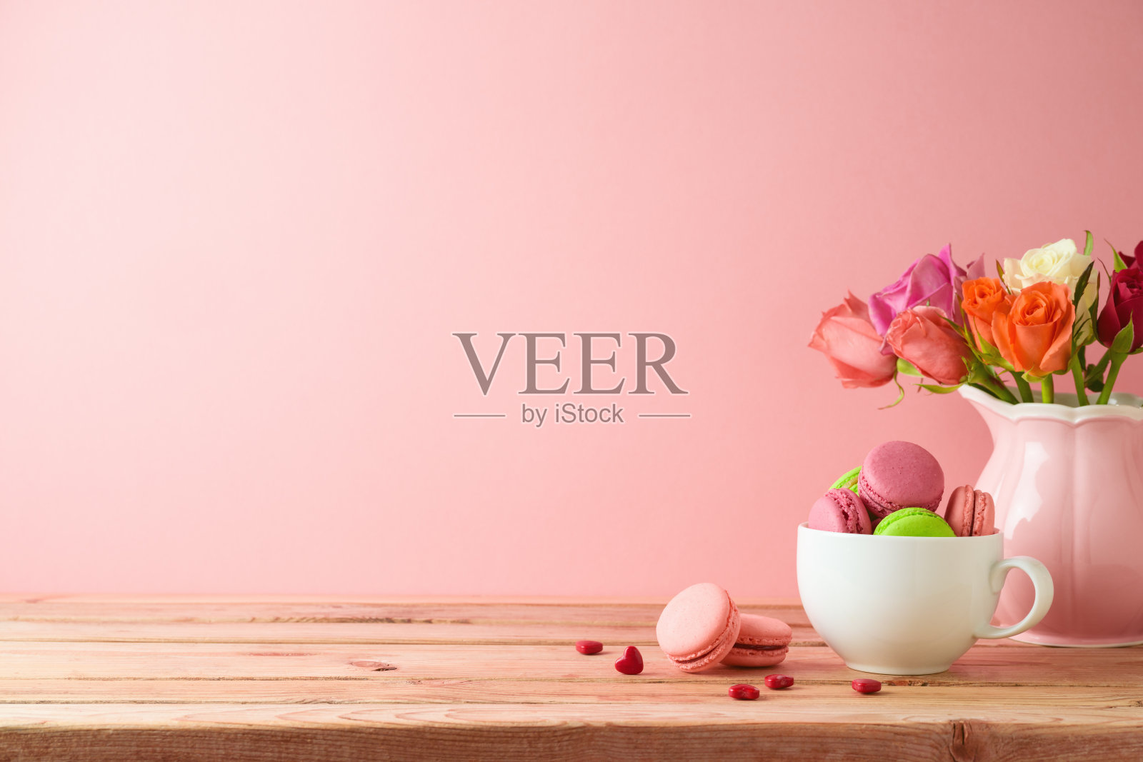 马卡龙法式曲奇放在木桌上，粉色背景上有玫瑰花束。照片摄影图片