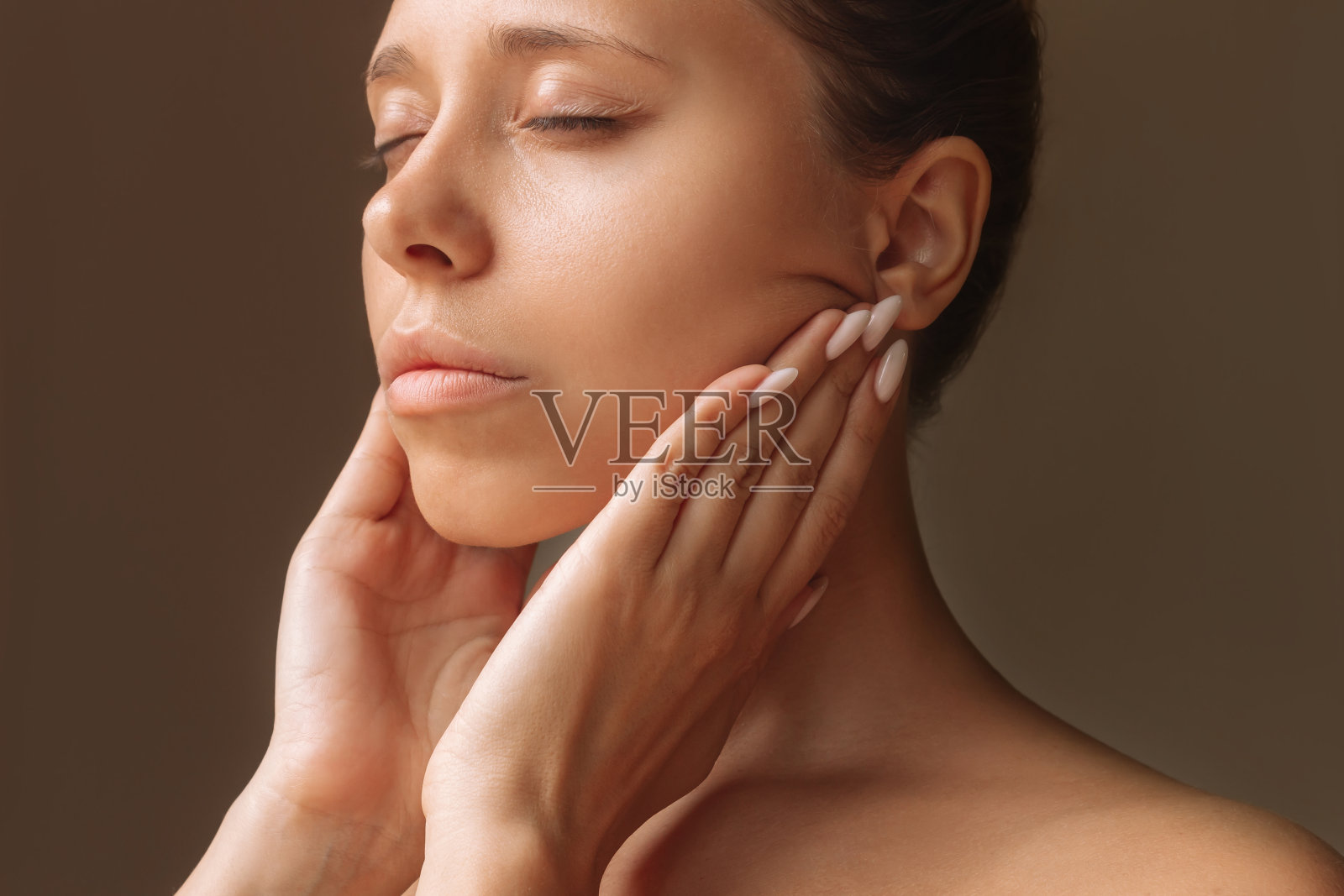 年轻女子触摸皮肤与手按摩她的脸。年轻化、拉皮、塑形照片摄影图片