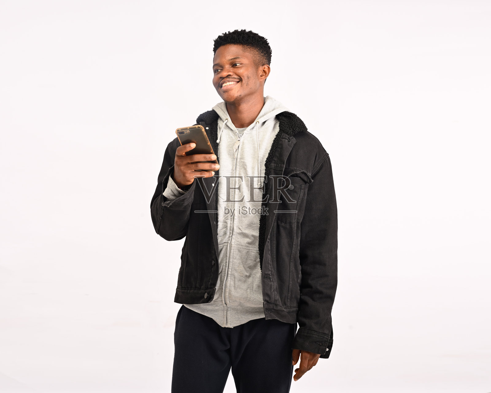 男孩在去见面地点的路上给女朋友发短信，手里拿着智能手机，笑着，笑得很可爱，看着设备屏幕，对白色墙壁上的可爱信息做出积极和快乐的反应照片摄影图片