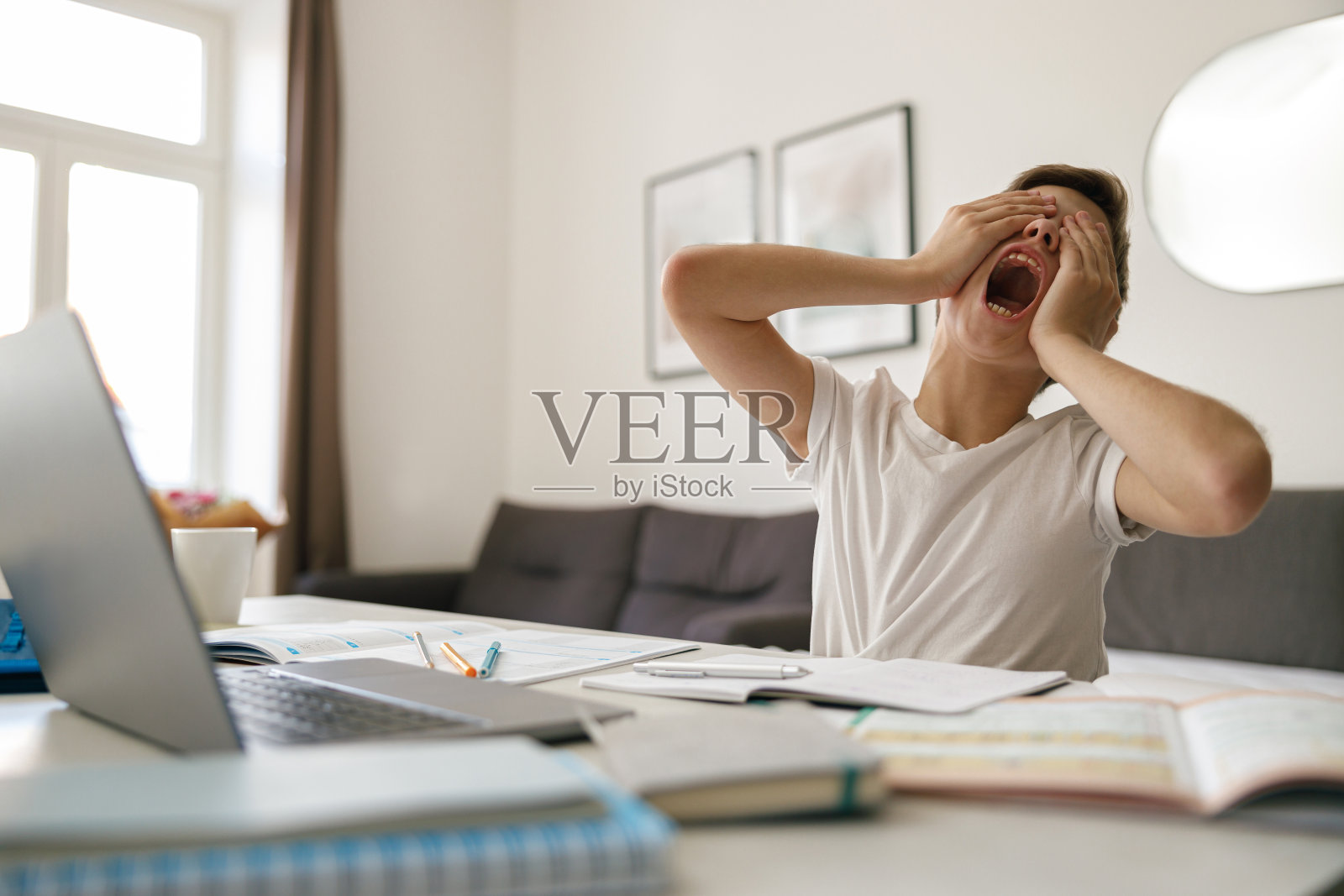 一个男孩在家里做作业时，一边打哈欠一边揉眼睛。儿童教育理念照片摄影图片