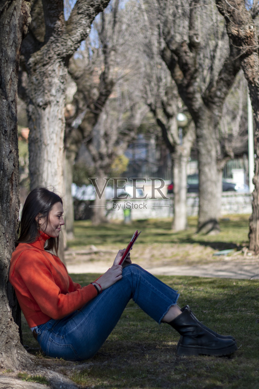 年轻的黑发女子坐在公园的草地上摆弄着平板电脑或电子设备照片摄影图片
